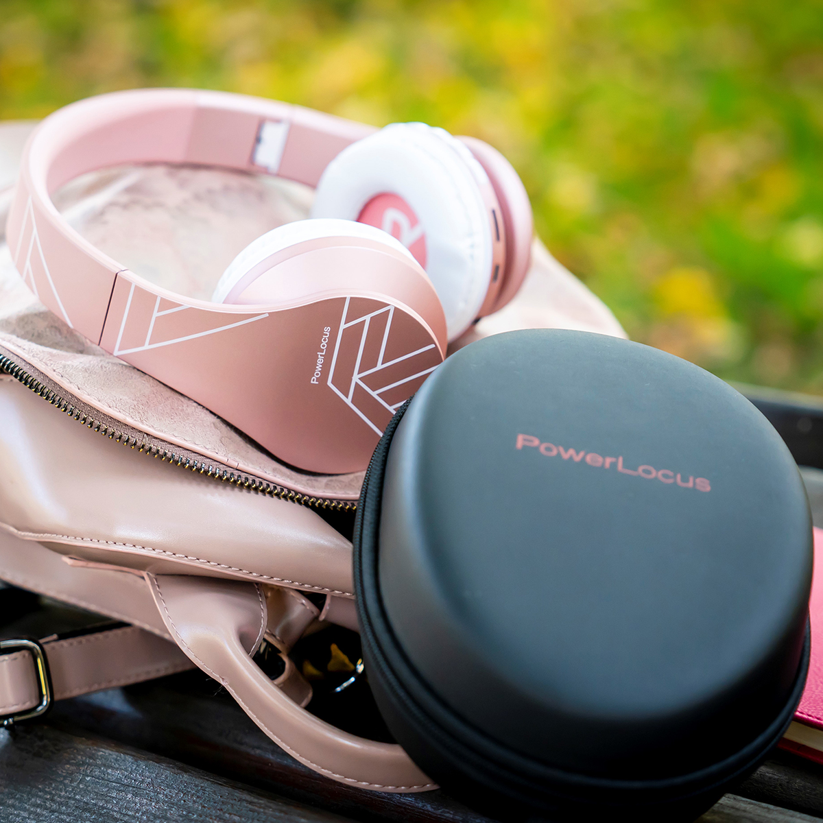 Cuffie e custodia rosa poggiano su una borsa rosa su una panchina di legno. Le cuffie hanno i padiglioni bianchi e la custodia è nera.