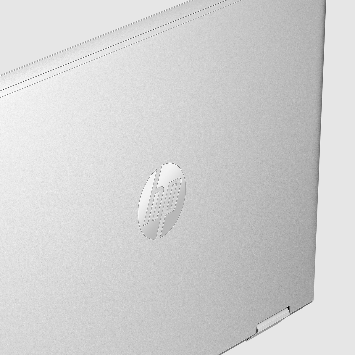 Zbliżenie srebrnej pokrywy laptopa. Widoczne logo HP. Pokrywa jest lekko otwarta, widać krawędź i białe tło.