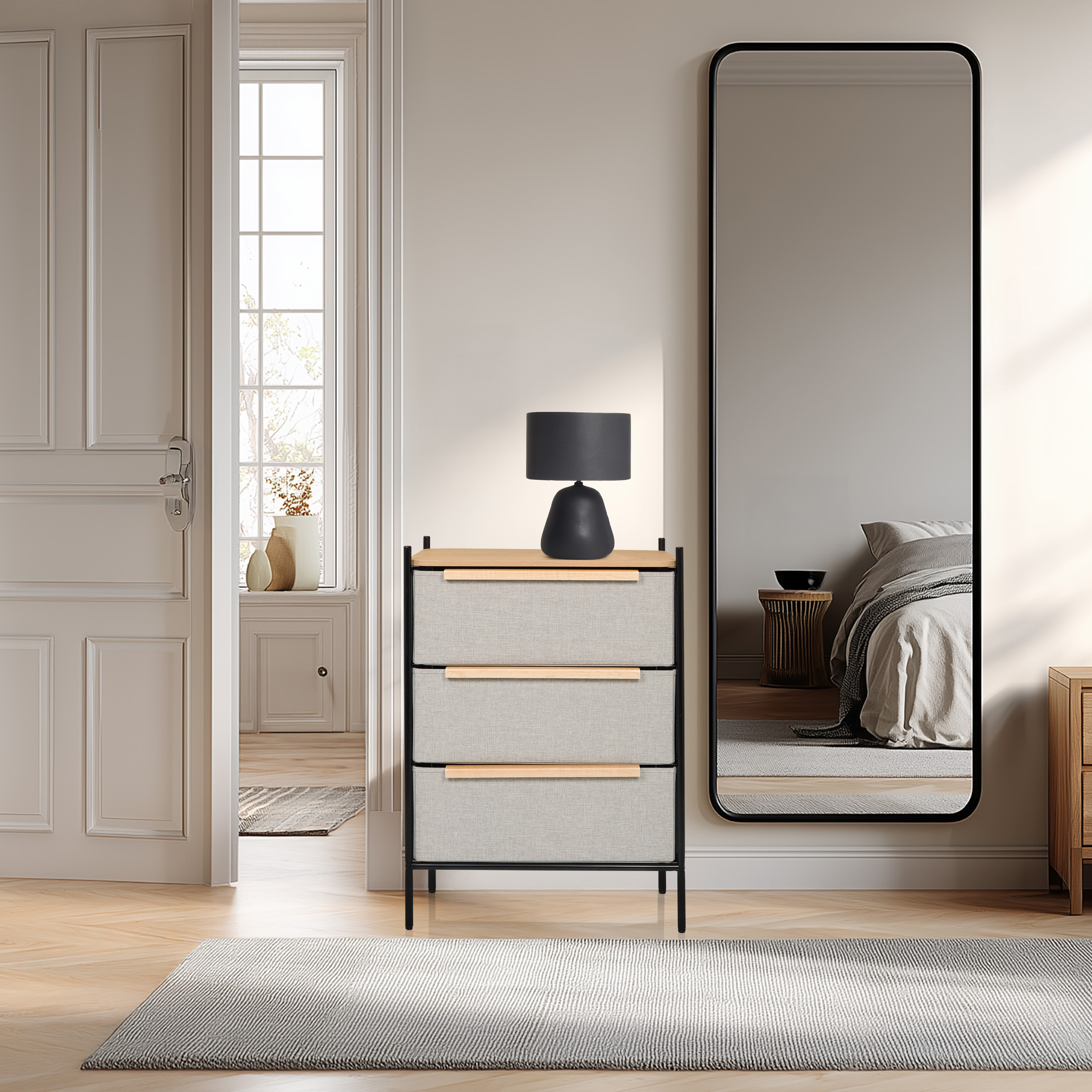 Ein Raum mit Kommode, Spiegel und Lampe. Ein Bett spiegelt sich im Spiegel. Eine Tür öffnet sich zu einem anderen Raum.