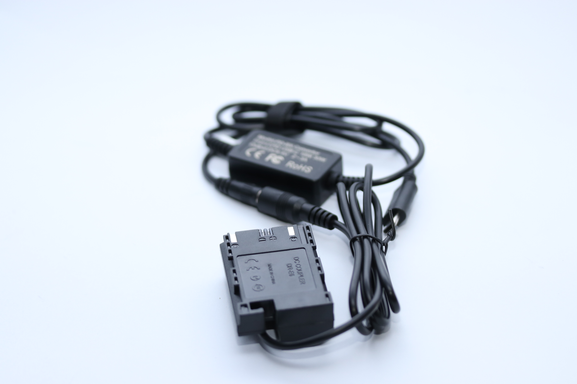 Schwarzer Kamera-Akku-Adapter mit Kabeln und Netzteil auf weißem Hintergrund. Der Adapter ist beschriftet.