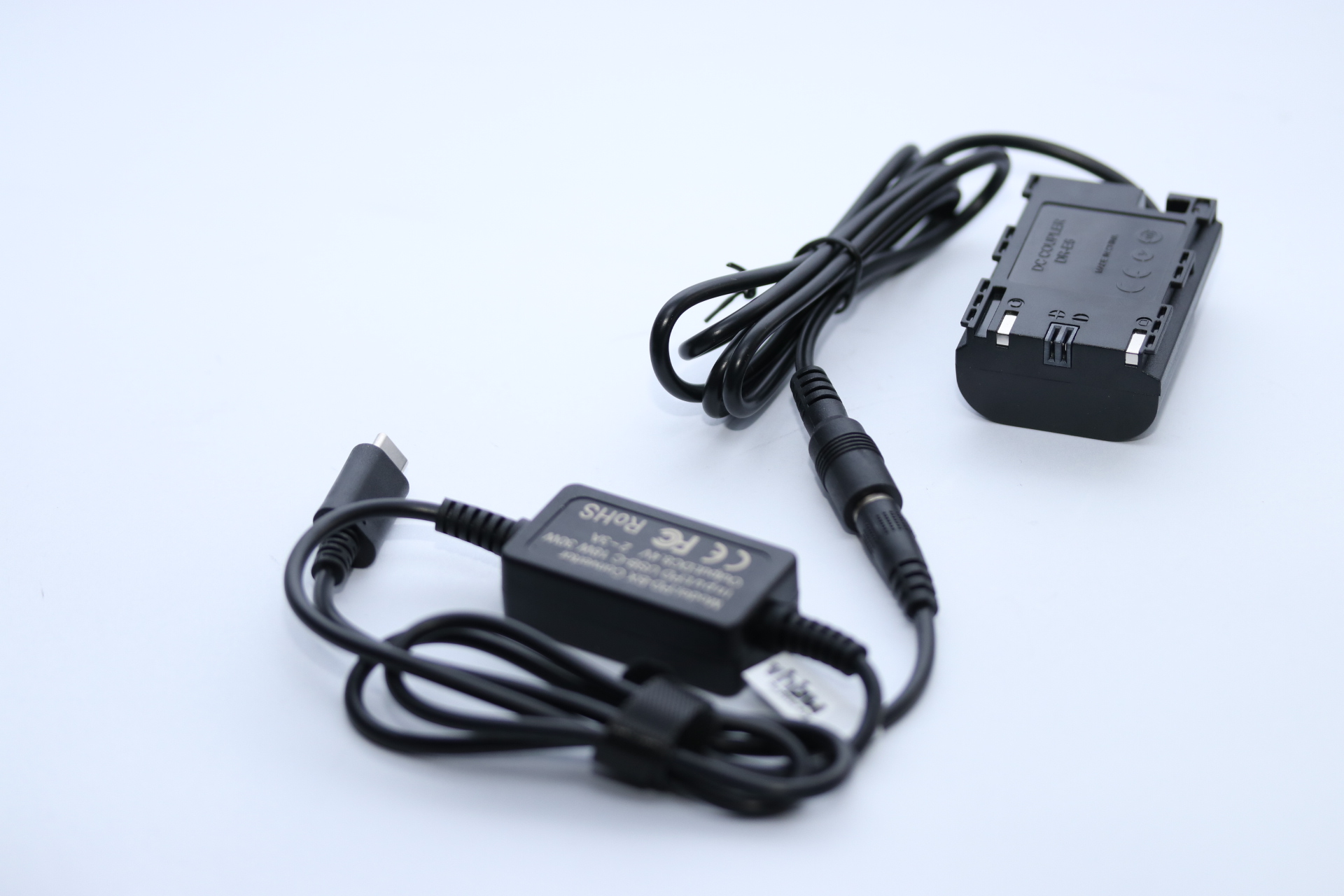 Schwarzer Gleichstrom-Koppler, USB-C-Kabel und Netzteil auf weißem Untergrund. Der Koppler ist mit 'DC Coupler DR-E6' beschriftet.