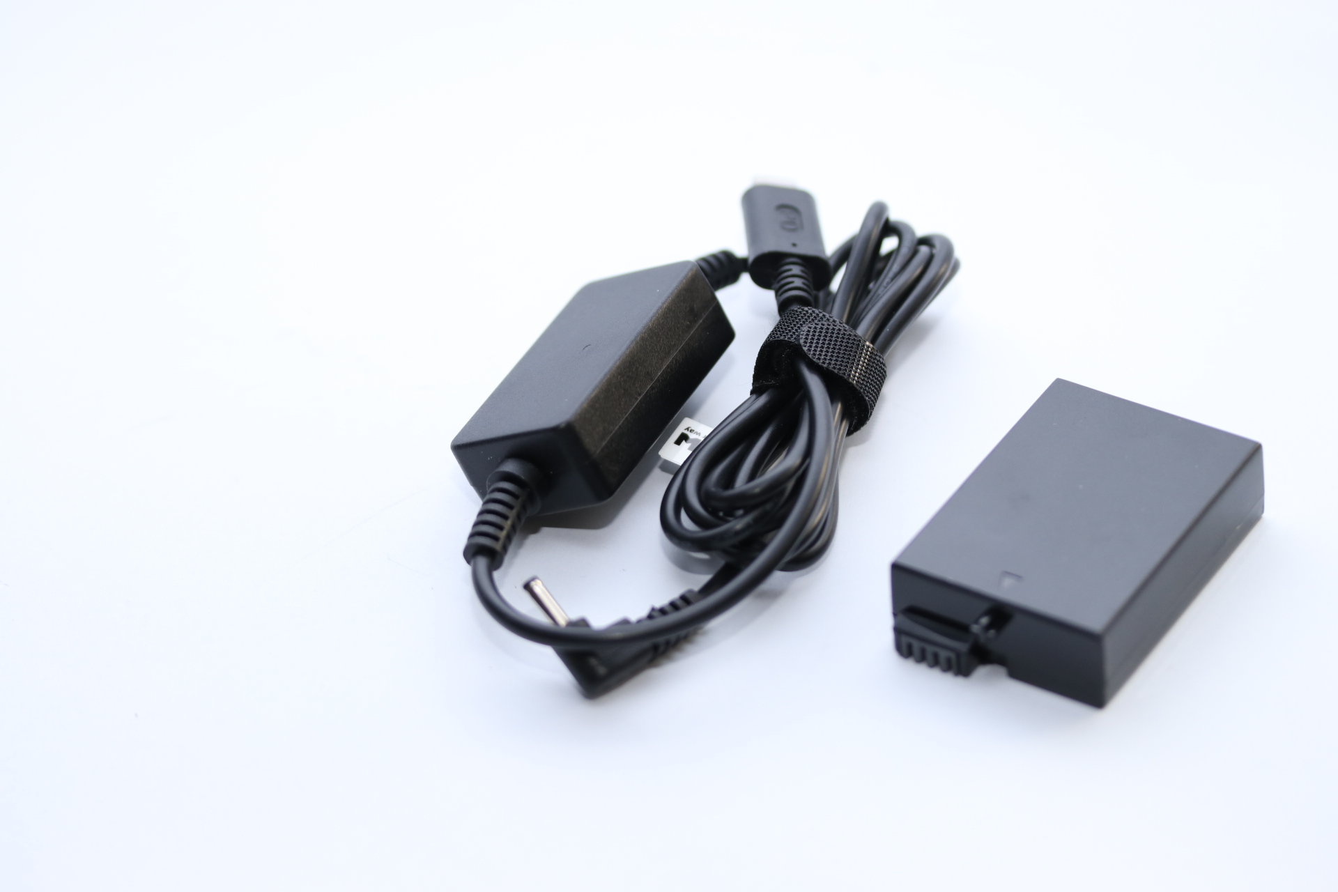 Ein schwarzes Netzteil mit Kabel liegt neben einem schwarzen Akkupack auf weißem Untergrund.