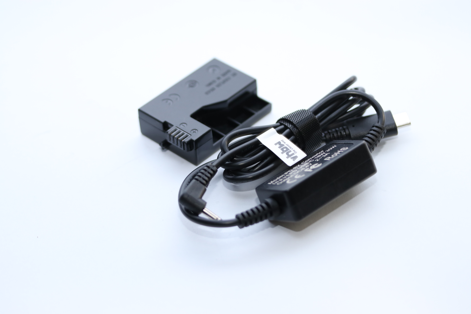 Schwarzer Akku und Ladegerät mit USB-Kabel auf weißer Oberfläche. Das Ladegerät hat ein Etikett und der Akku einen Anschluss.