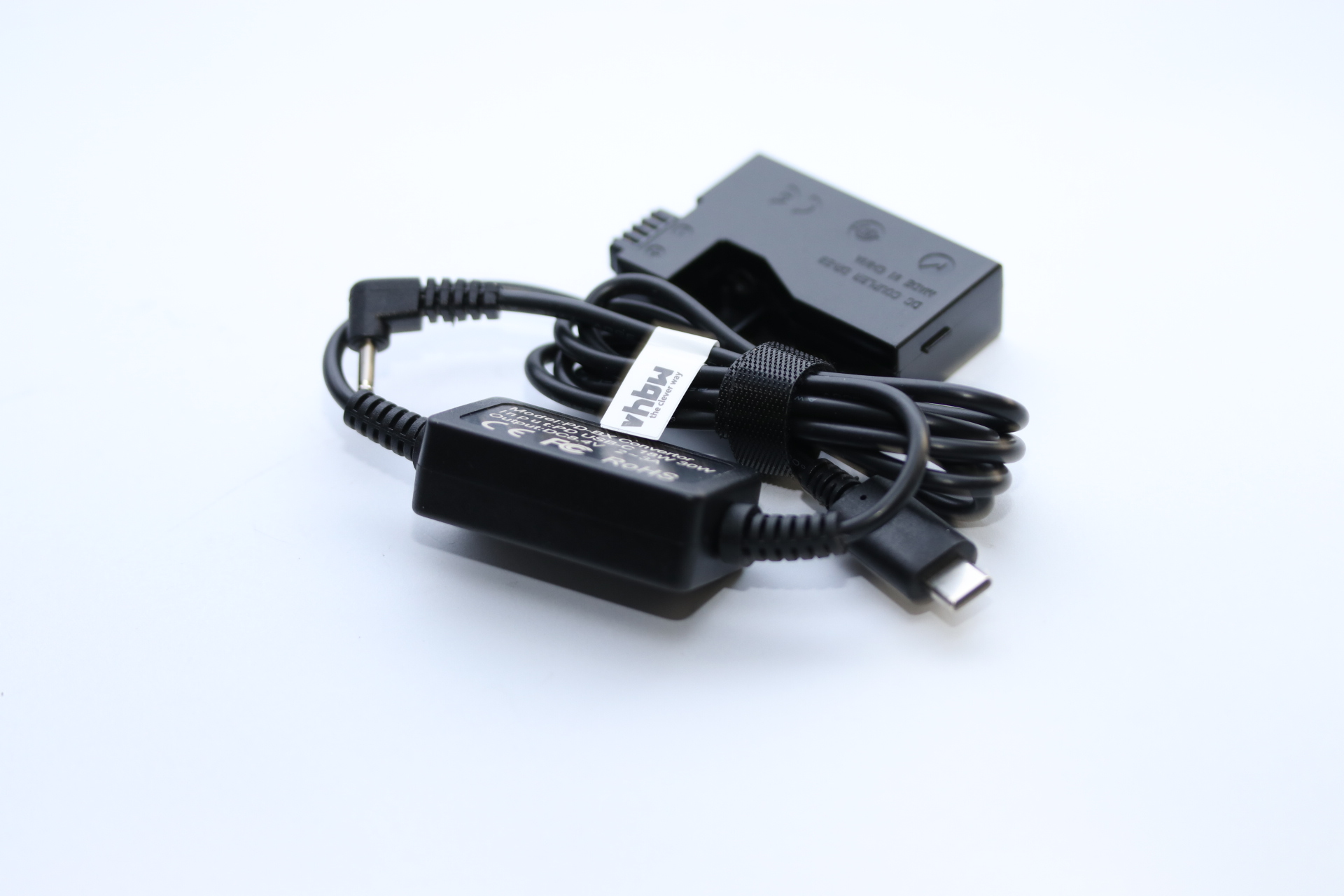 Ein schwarzer DC-Koppler mit Kabeln, einem USB-C-Anschluss und einem Etikett. Es liegt auf einer weißen Oberfläche.