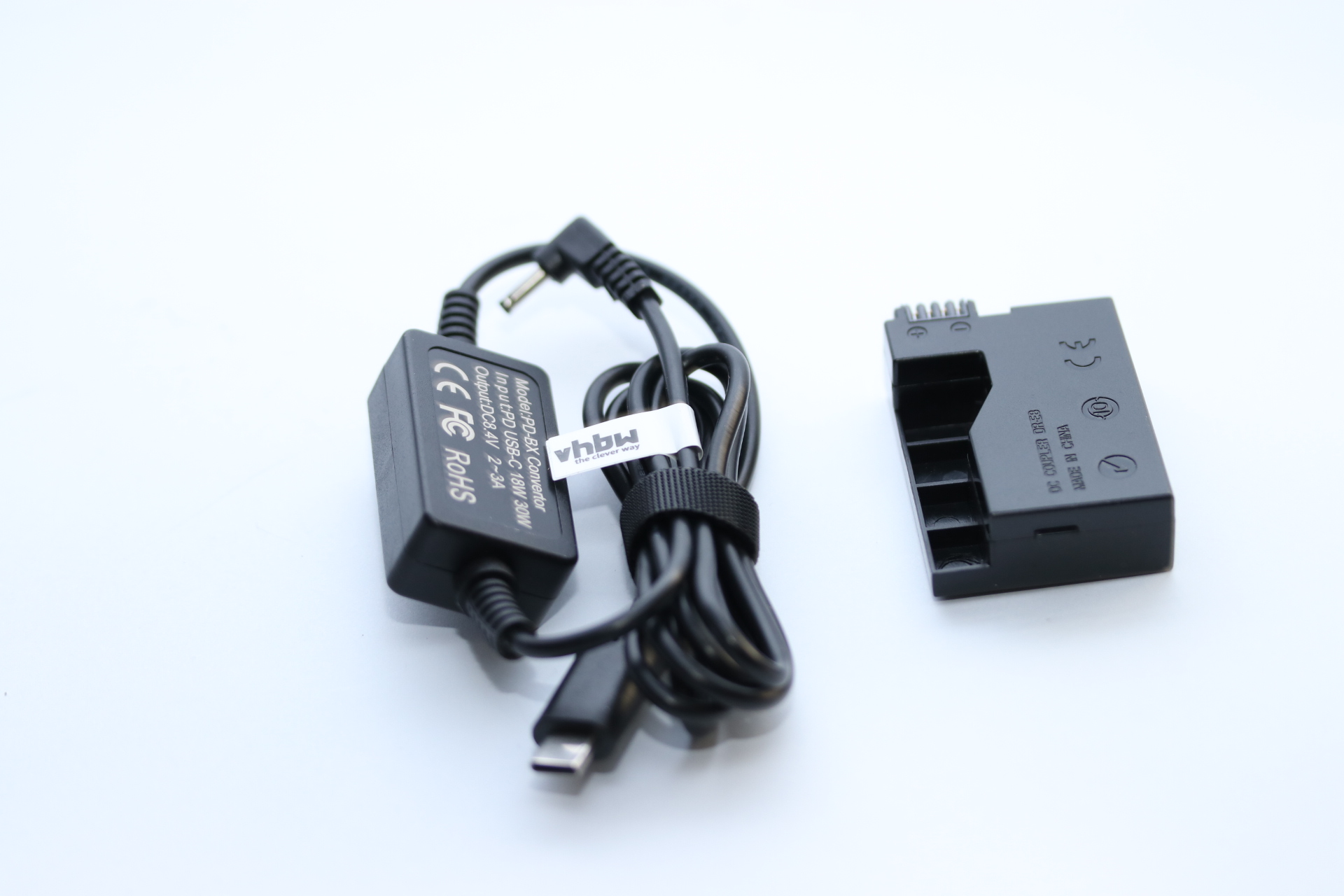 Schwarzer Adapter mit USB-C-Kabel und eine weitere schwarze Komponente auf weißer Oberfläche. Text auf dem Adapter zeigt Spannung und Marke.