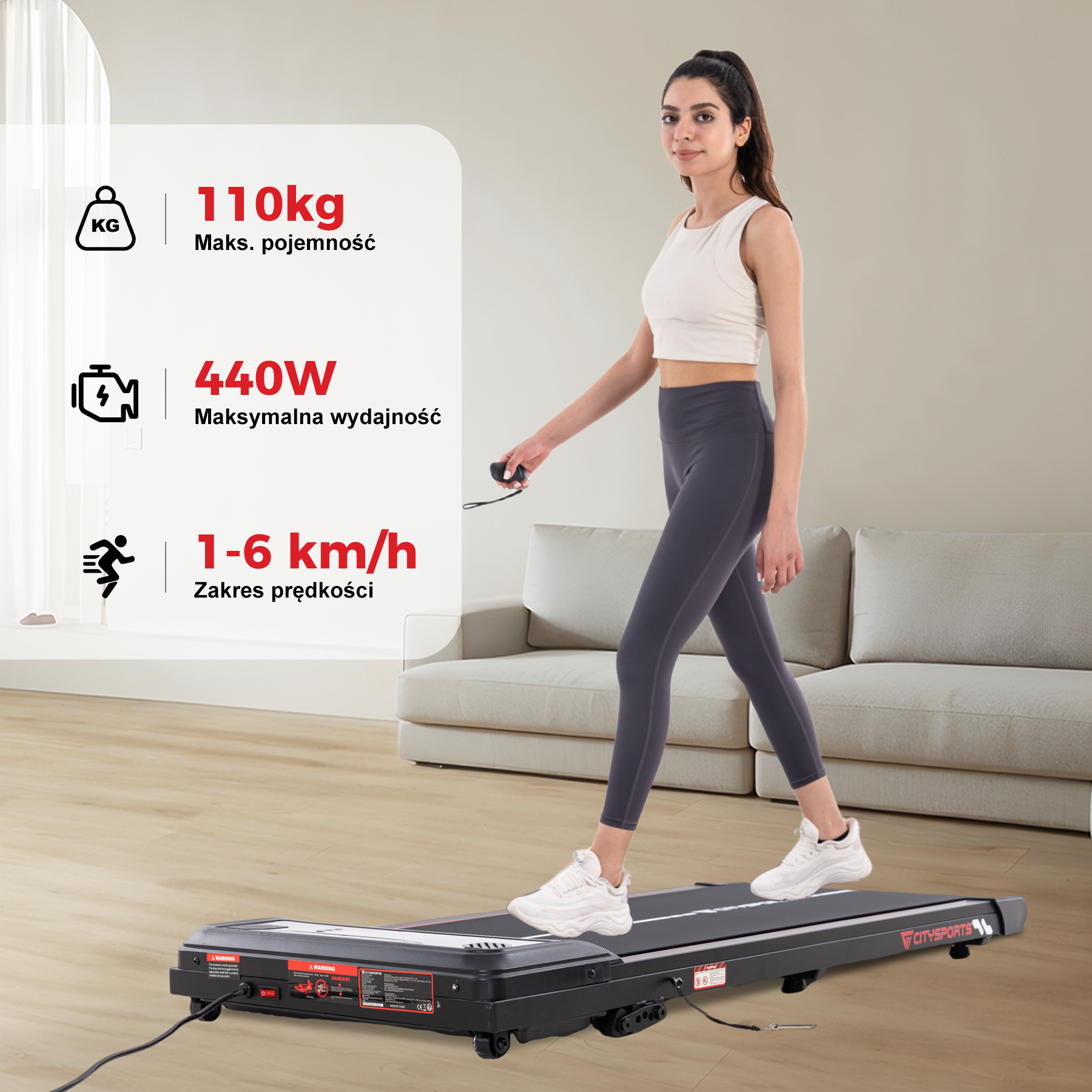 Kobieta spaceruje na bieżni. Ma pojemność 110 kg, moc 440 W i zakres prędkości 1-6 km/h. W tle sofa.