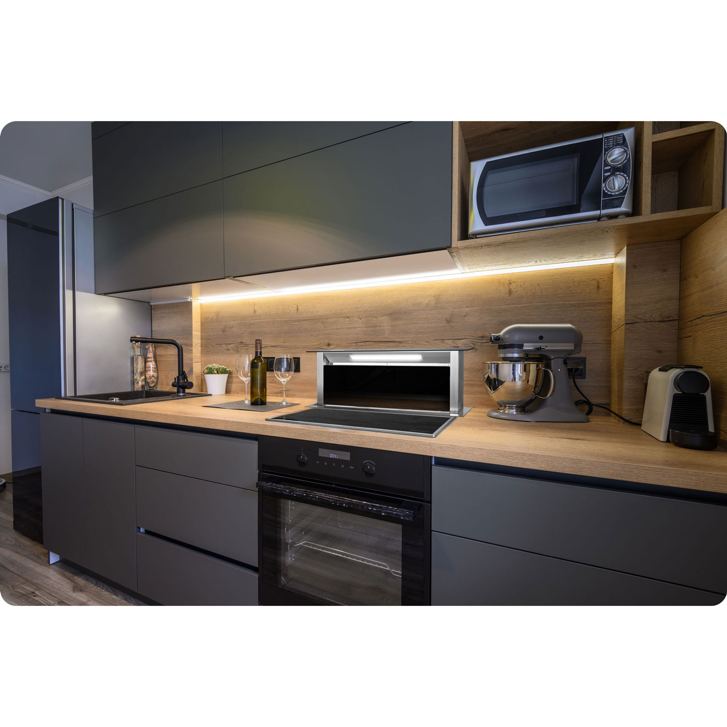 Nowoczesna kuchnia z szarymi szafkami, drewnianym blatem. Zawiera piekarnik, kuchenkę mikrofalową, mikser, wino i płytę grzewczą.