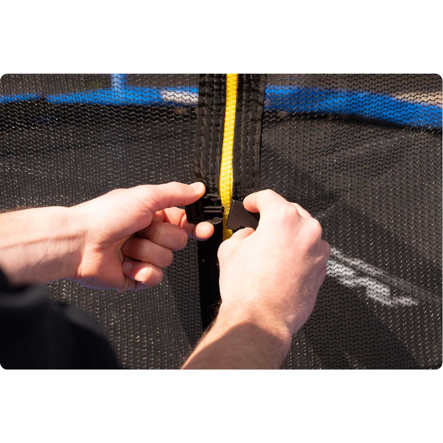 Ręce zabezpieczające czarny zamek błyskawiczny siatki bezpieczeństwa na trampolinie. Żółty zamek i czarna siatka widoczne.