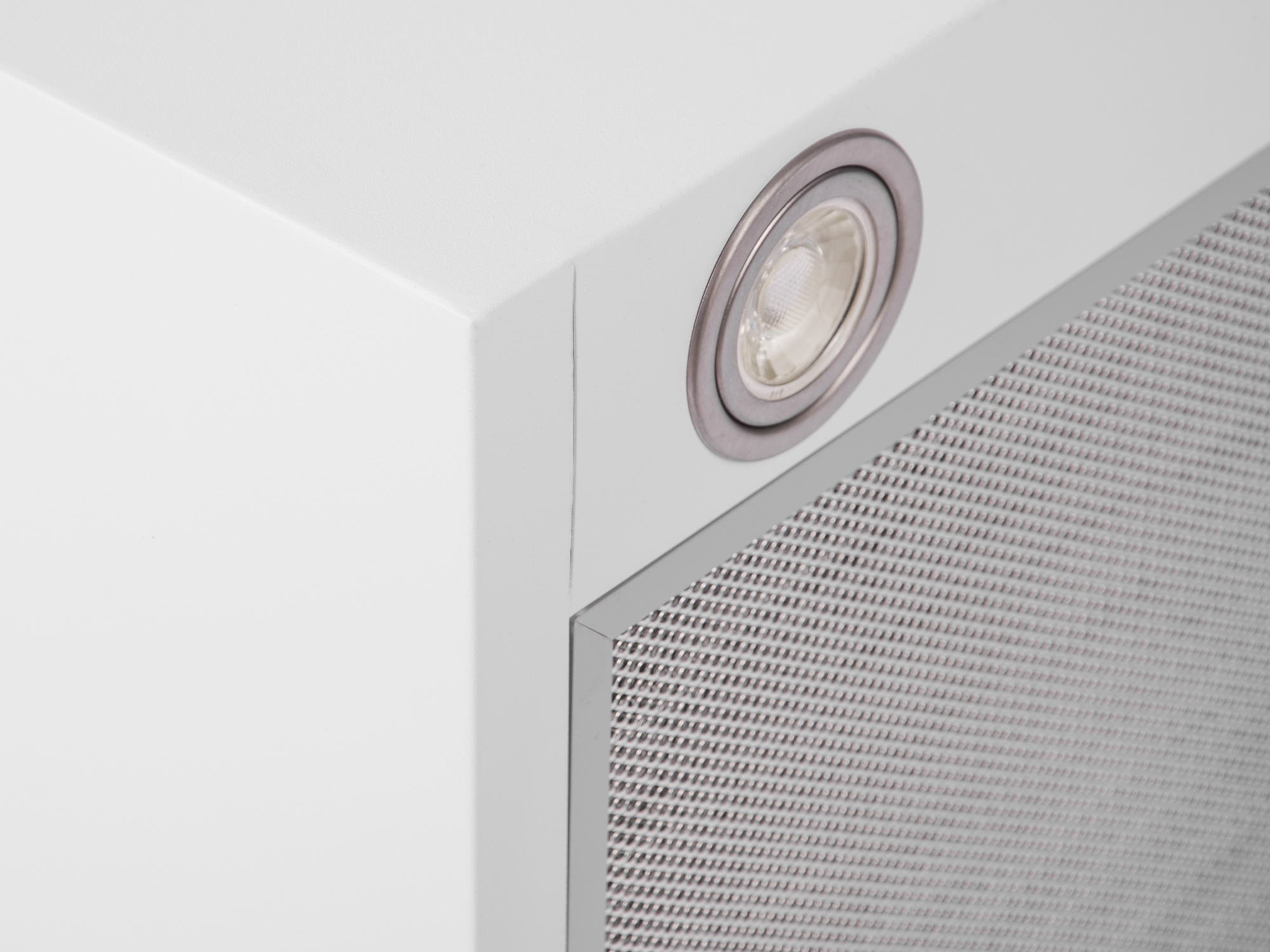 Zbliżenie białego rogu okapu z światłem i metalowym filtrem siatkowym. Światło jest okrągłe ze srebrną obwódką.