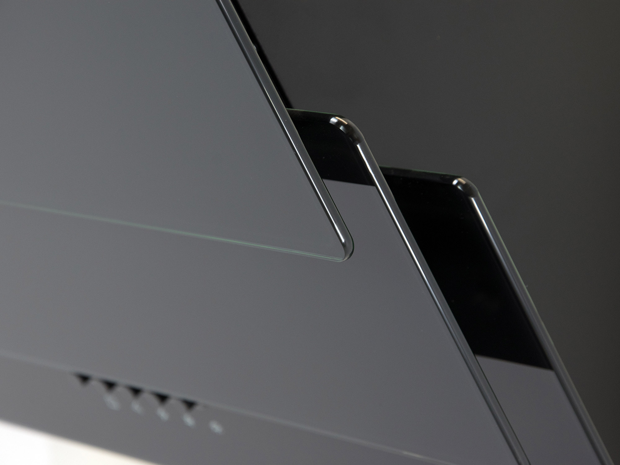 Zbliżenie czarnego, błyszczącego obiektu z ostrymi kątami. Powierzchnia odbija światło. Na dole znajduje się kilka małych otworów.