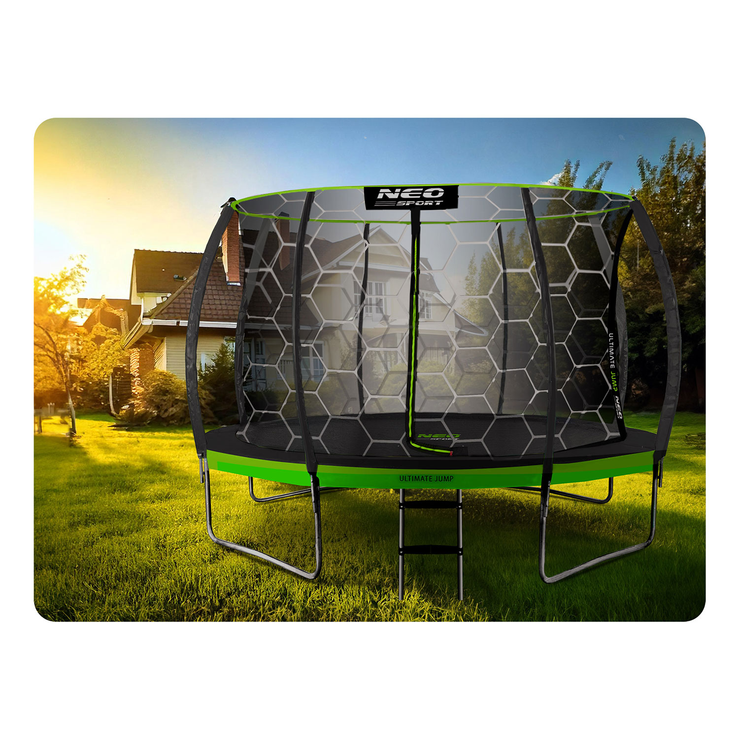 Trampolina z siatką zabezpieczającą na zielonym trawniku. W tle domy i drzewa. Błękitne niebo z zachodzącym słońcem.