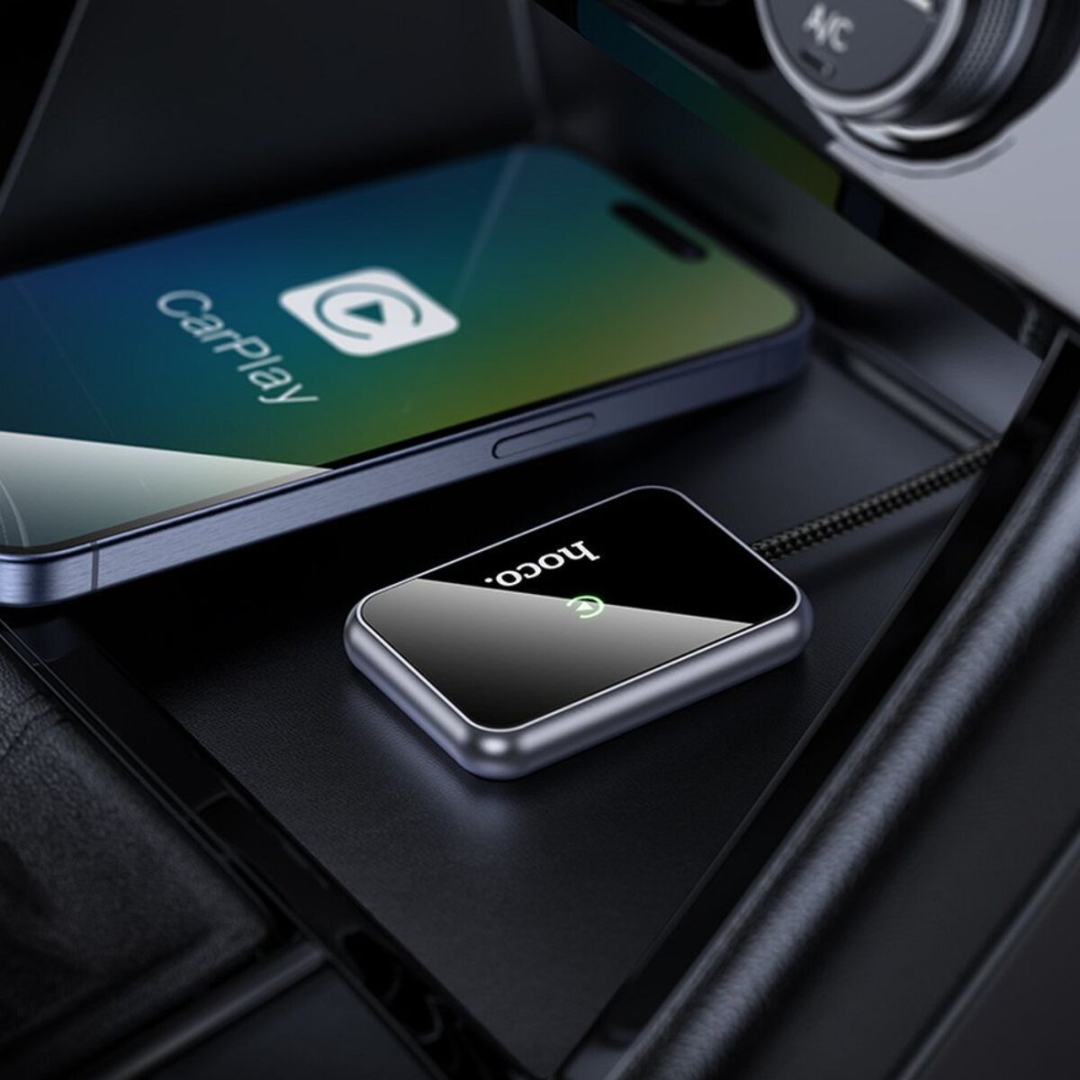 Un smartphone con CarPlay junto a un dispositivo negro con el logotipo de Hoco, conectado por cable, dentro de un coche.