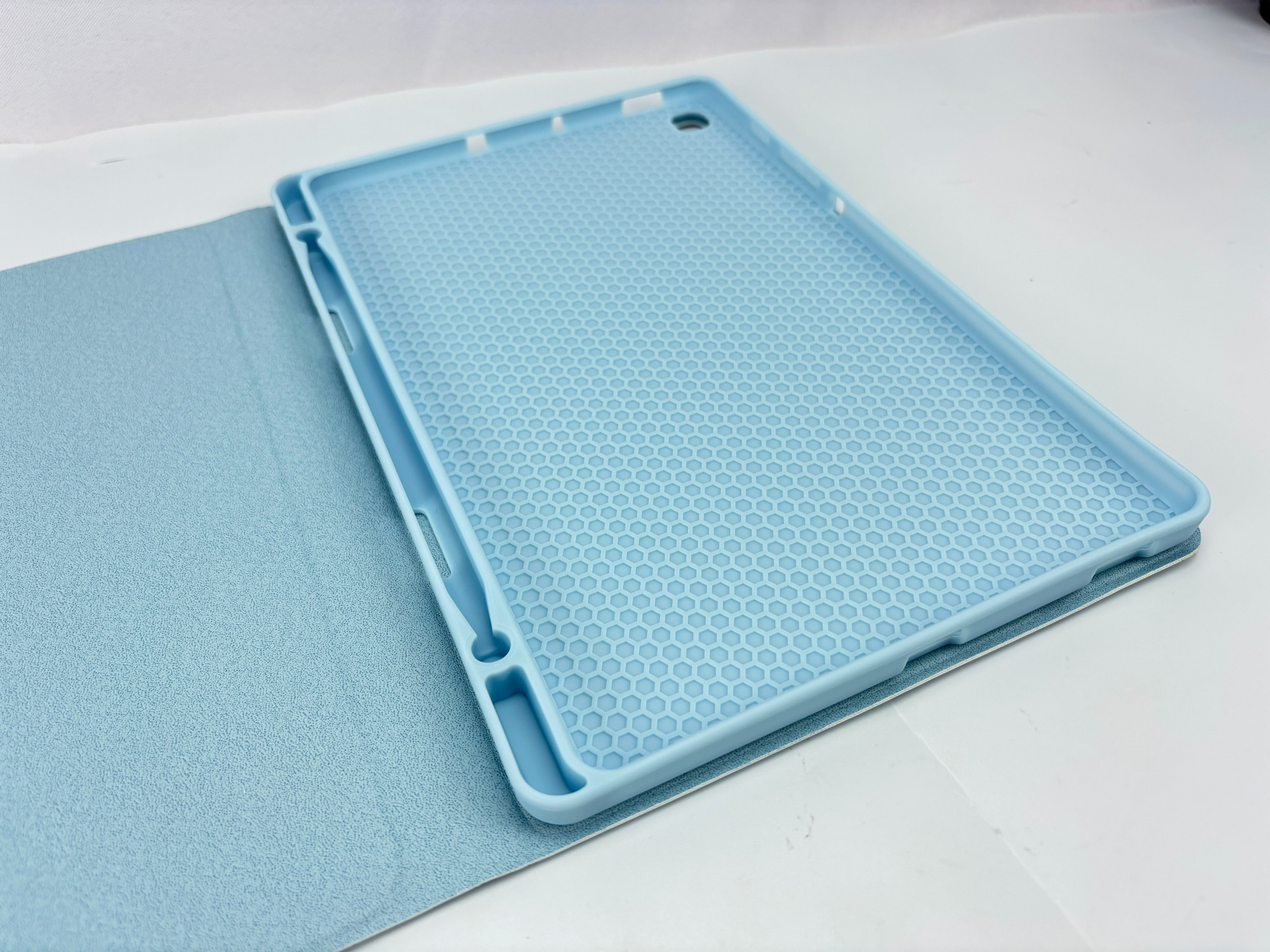 Eine hellblaue Tablethülle ist auf einer weißen Oberfläche geöffnet. Die Hülle hat innen ein Wabenmuster. Der Hintergrund ist weiß.