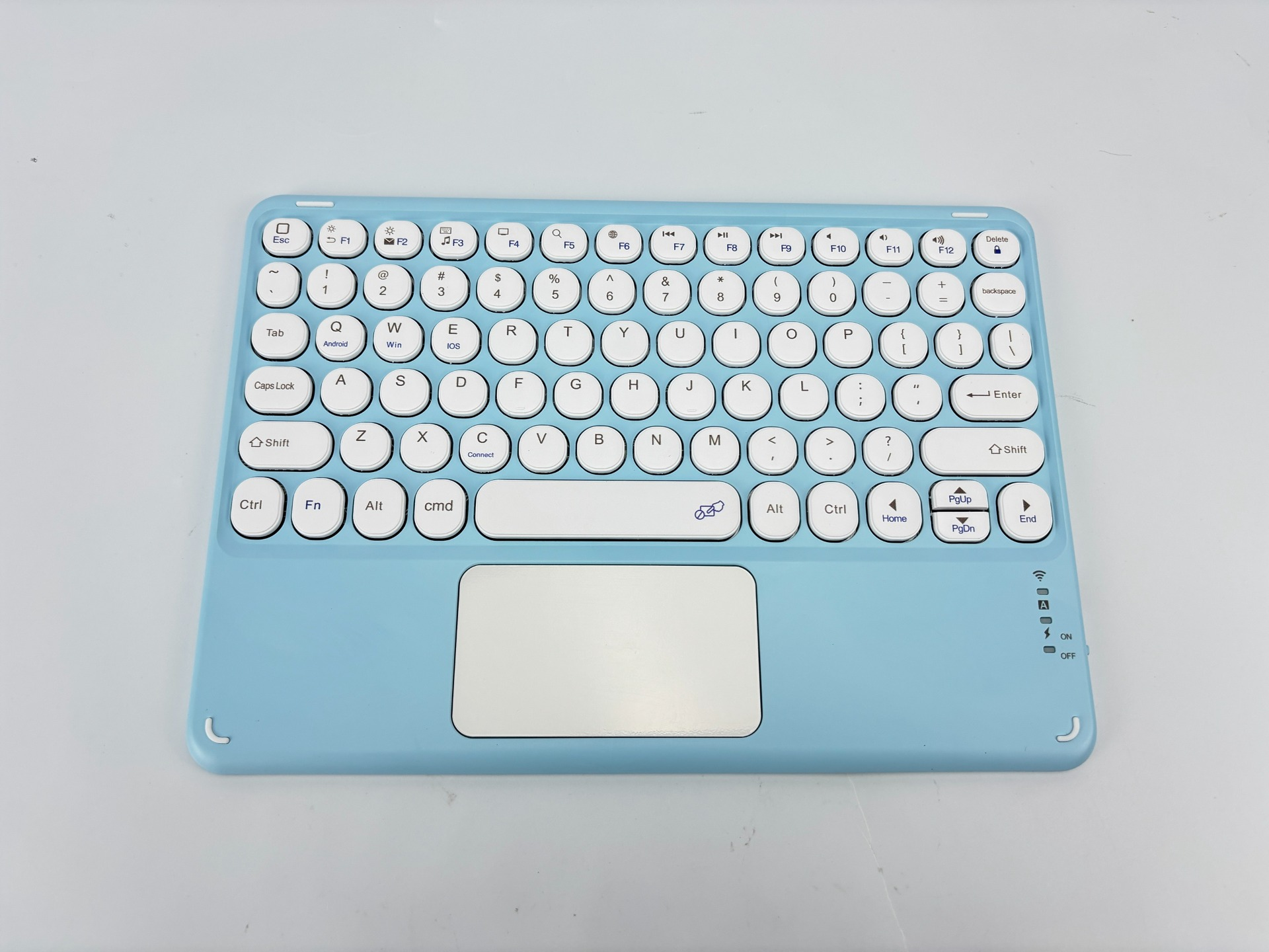Eine hellblaue kabellose Tastatur mit weißen Tasten, einem Touchpad und Funktionstasten, die auf einer weißen Oberfläche liegt.