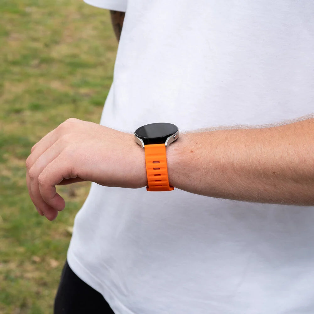 Eine Person trägt eine orangefarbene Smartwatch am Handgelenk. Die Uhr hat einen schwarzen Bildschirm und ein silbernes Gehäuse. Sie tragen ein weißes Hemd.