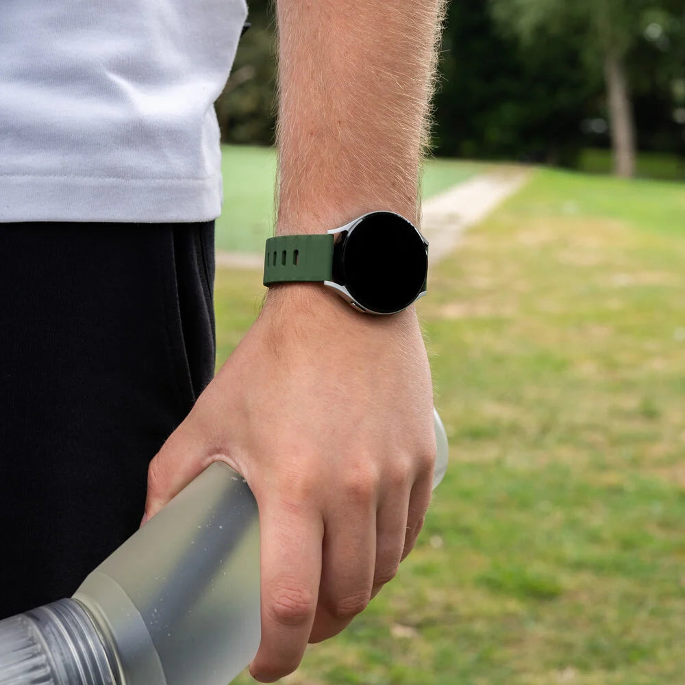 Eine Person mit Smartwatch am Handgelenk hält eine Wasserflasche. Der Hintergrund ist eine verschwommene grüne Wiese.