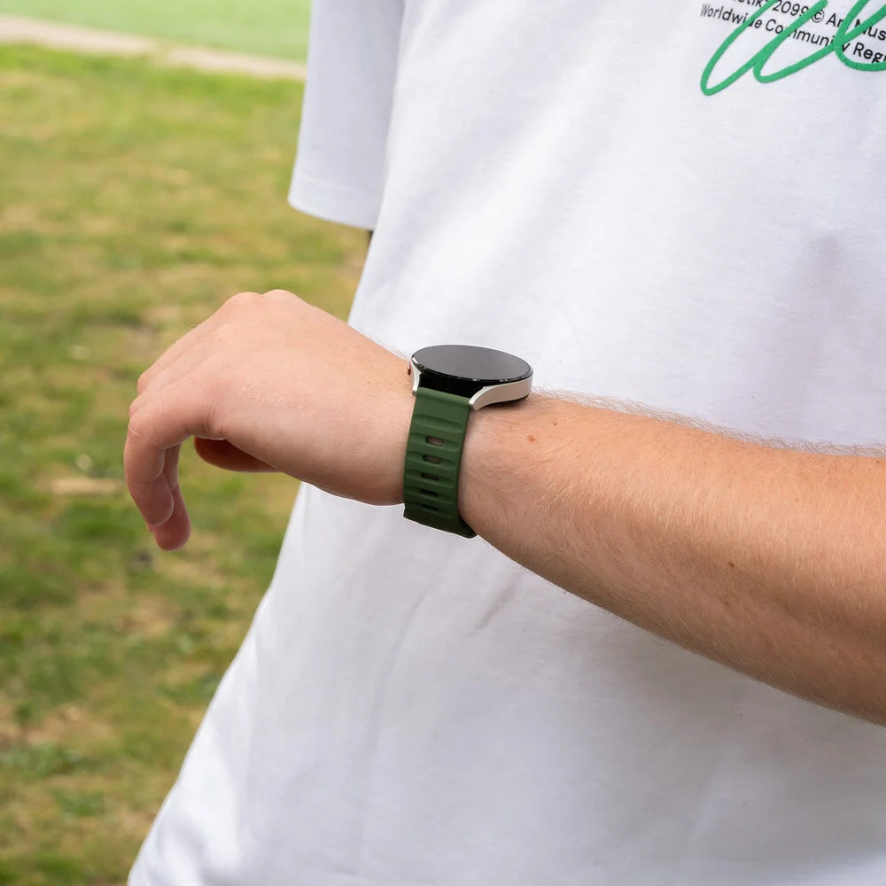 Person trägt Smartwatch mit grünem Armband. Die Uhr befindet sich am linken Handgelenk. Die Person trägt ein weißes Hemd.