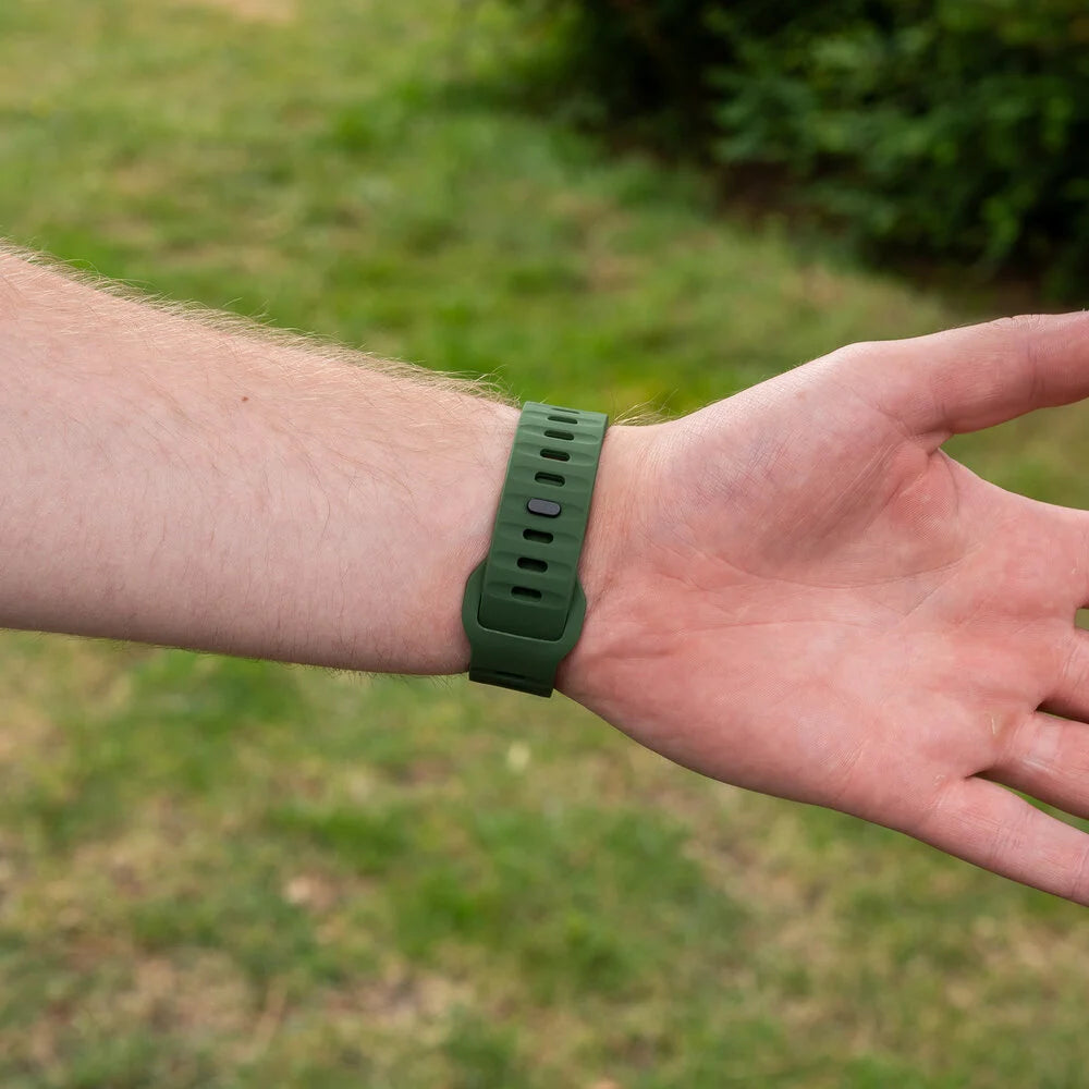 Ein Arm mit einem grünen Armband. Im Hintergrund ein verschwommener grüner Rasen und Bäume.