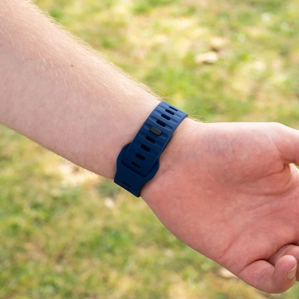 Ein Handgelenk mit einem dunkelblauen Armband. Der Hintergrund ist grünes Gras.