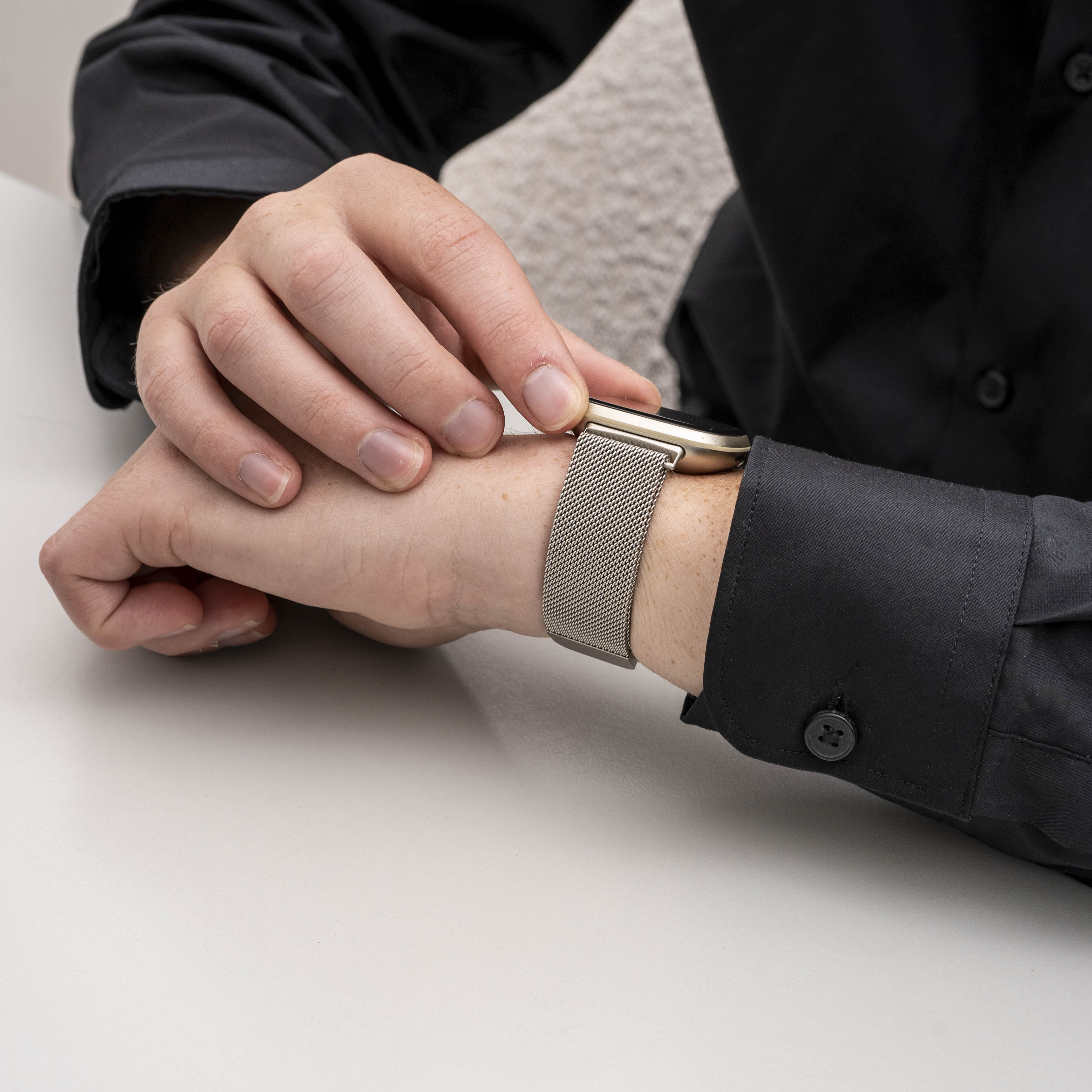 Eine Person in einem schwarzen Hemd stellt eine Uhr an ihrem Handgelenk ein. Die Uhr hat ein Metallband und ein goldfarbenes Zifferblatt.