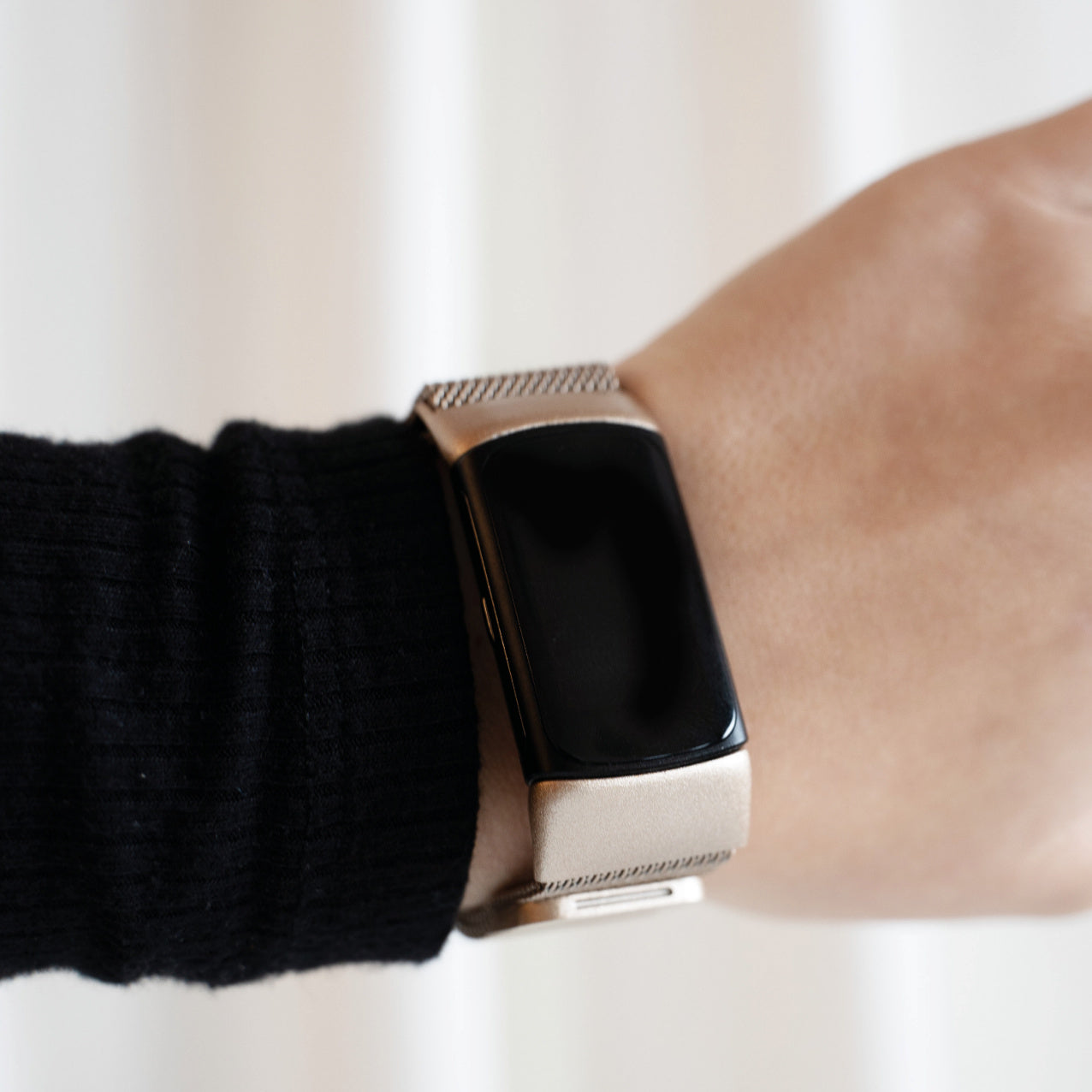 Eine Person, die eine Smartwatch mit schwarzem Bildschirm und einem silber-goldenen Armband trägt. Die Person trägt einen schwarzen Pullover.
