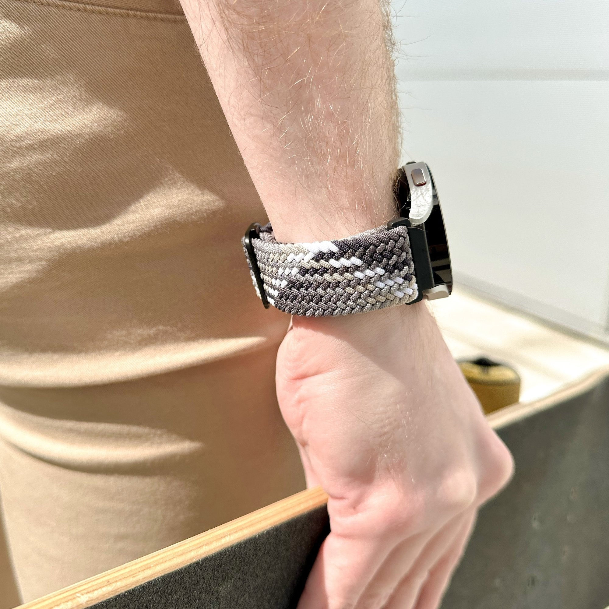 Ein Arm mit Uhr und gemustertem Band. Er hält ein Skateboard. Neutrale Töne dominieren das Bild.
