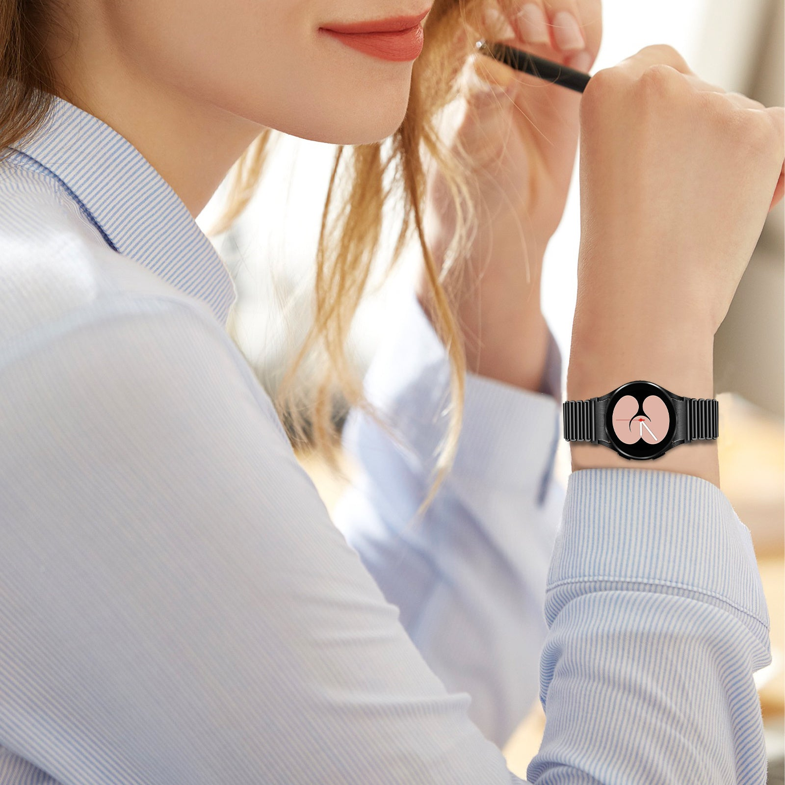 Frau mit Smartwatch am Handgelenk. Sie hält einen Stift. Die Uhr hat ein schwarzes Armband und ein rosa Display.