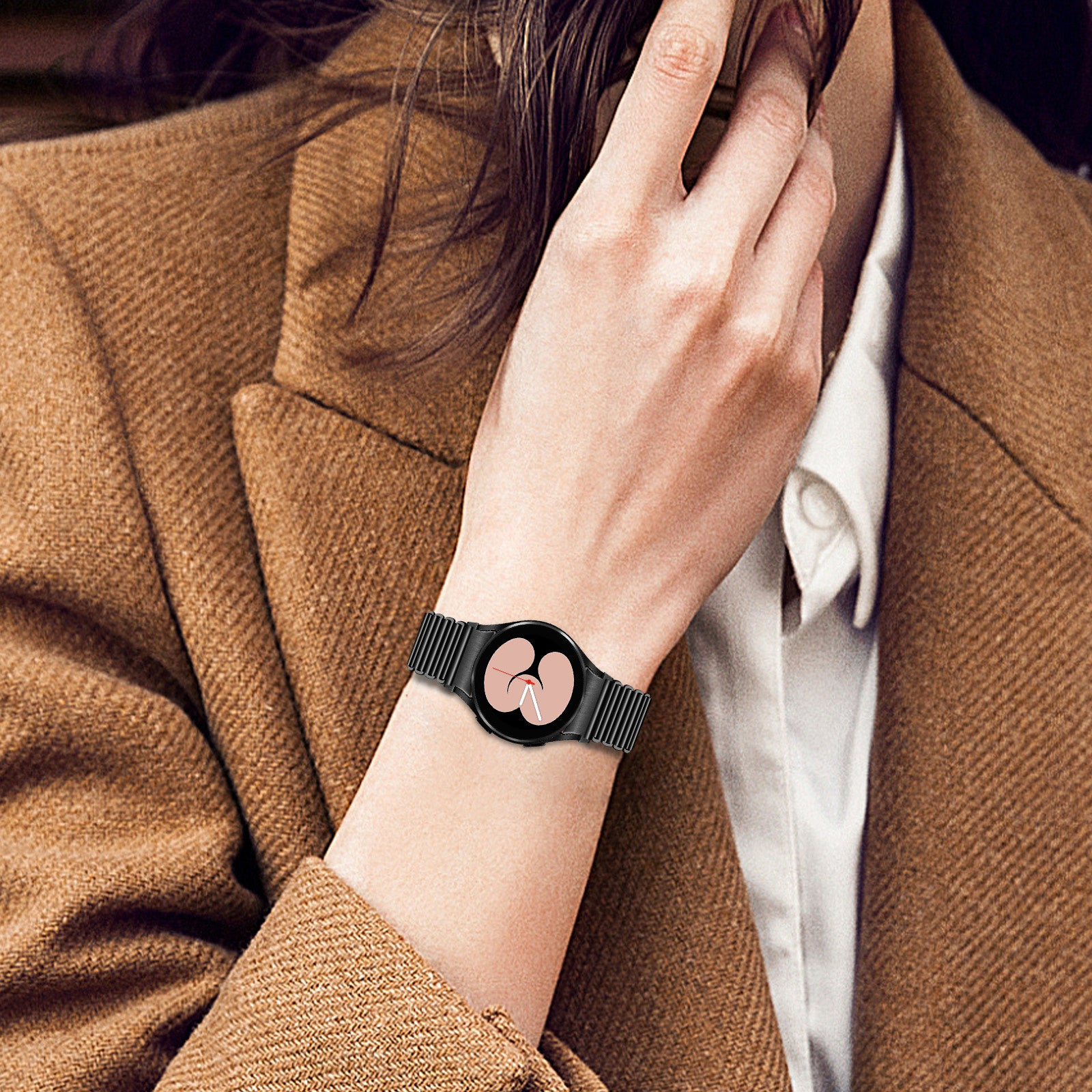Eine Person, die eine schwarze Smartwatch mit rosa Bildschirm trägt. Sie trägt einen braunen Mantel und ein weißes Hemd.