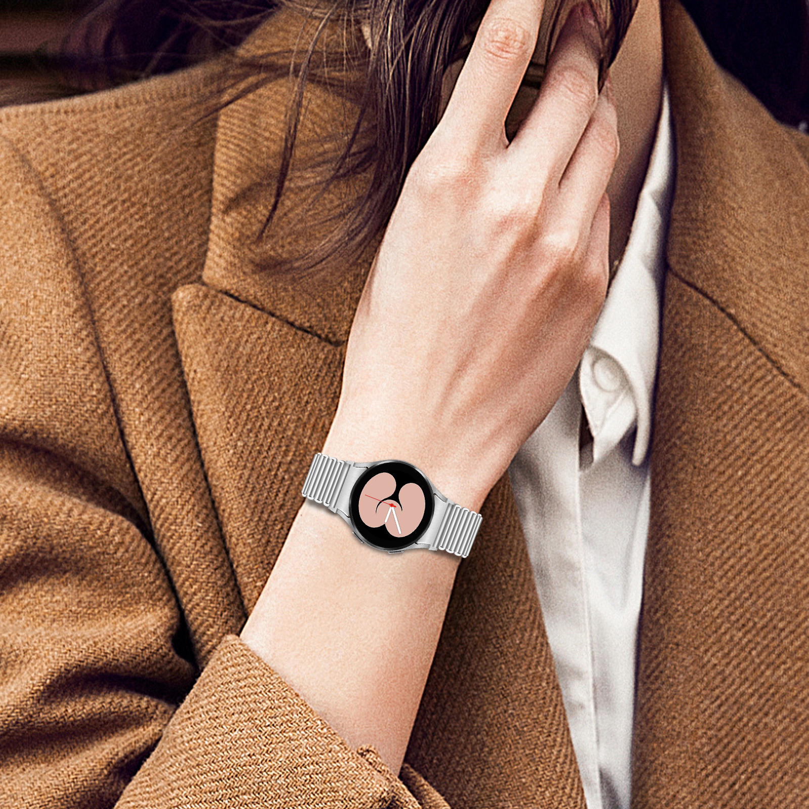 Eine Person, die eine silberne Uhr am Handgelenk trägt, mit einem braunen Mantel und einem weißen Hemd. Hand berührt das Gesicht.