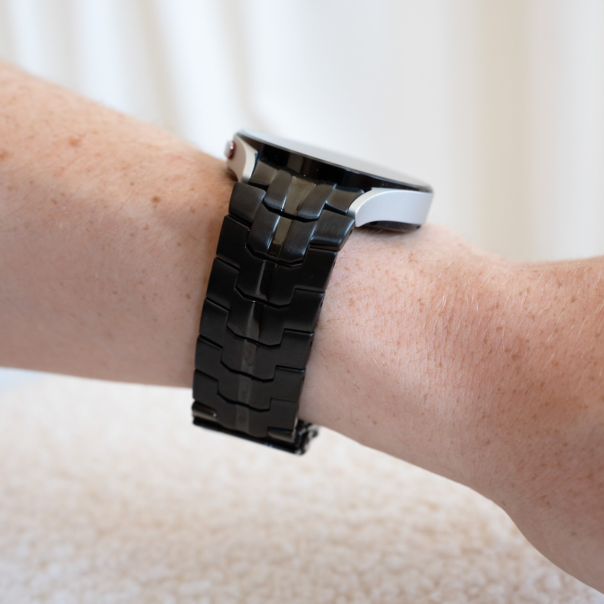 Eine schwarze Uhr befindet sich am Arm einer Person. Der Arm hat helle Haut mit Sommersprossen. Der Hintergrund ist unscharf.
