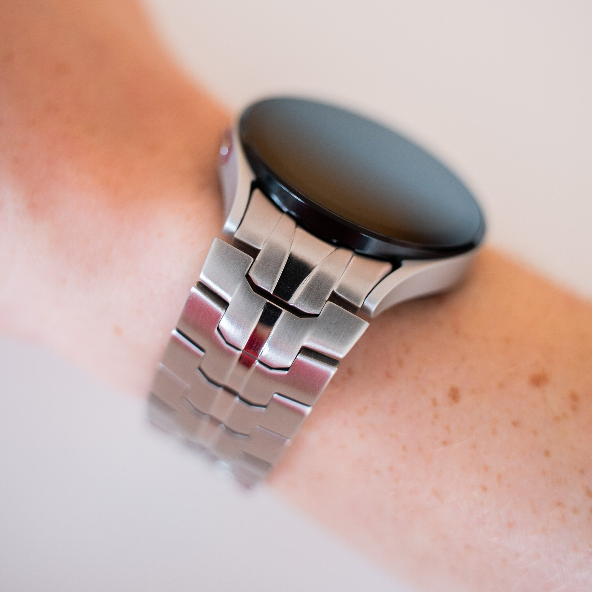 Eine silberne Smartwatch am Handgelenk. Die Uhr hat einen schwarzen Bildschirm und ein silbernes Metallband. Haut ist sichtbar.