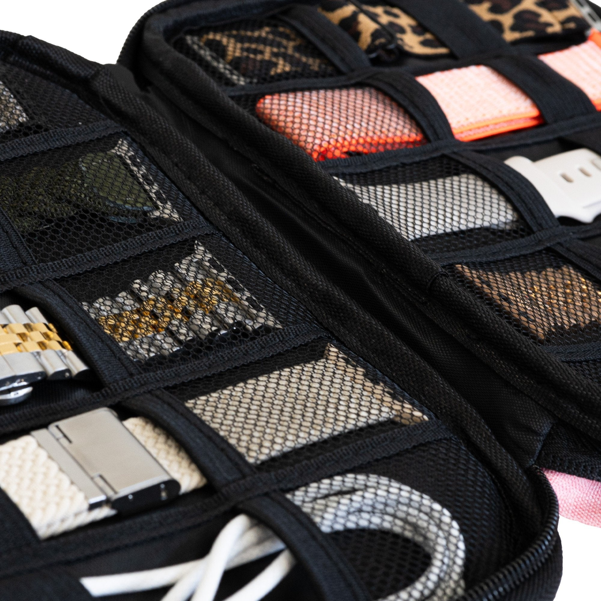 Schwarzer Organizer mit Fächern, die Uhrenarmbänder, Kabel und anderes Zubehör enthalten. Leopard- und pfirsichfarbene Träger sind sichtbar.
