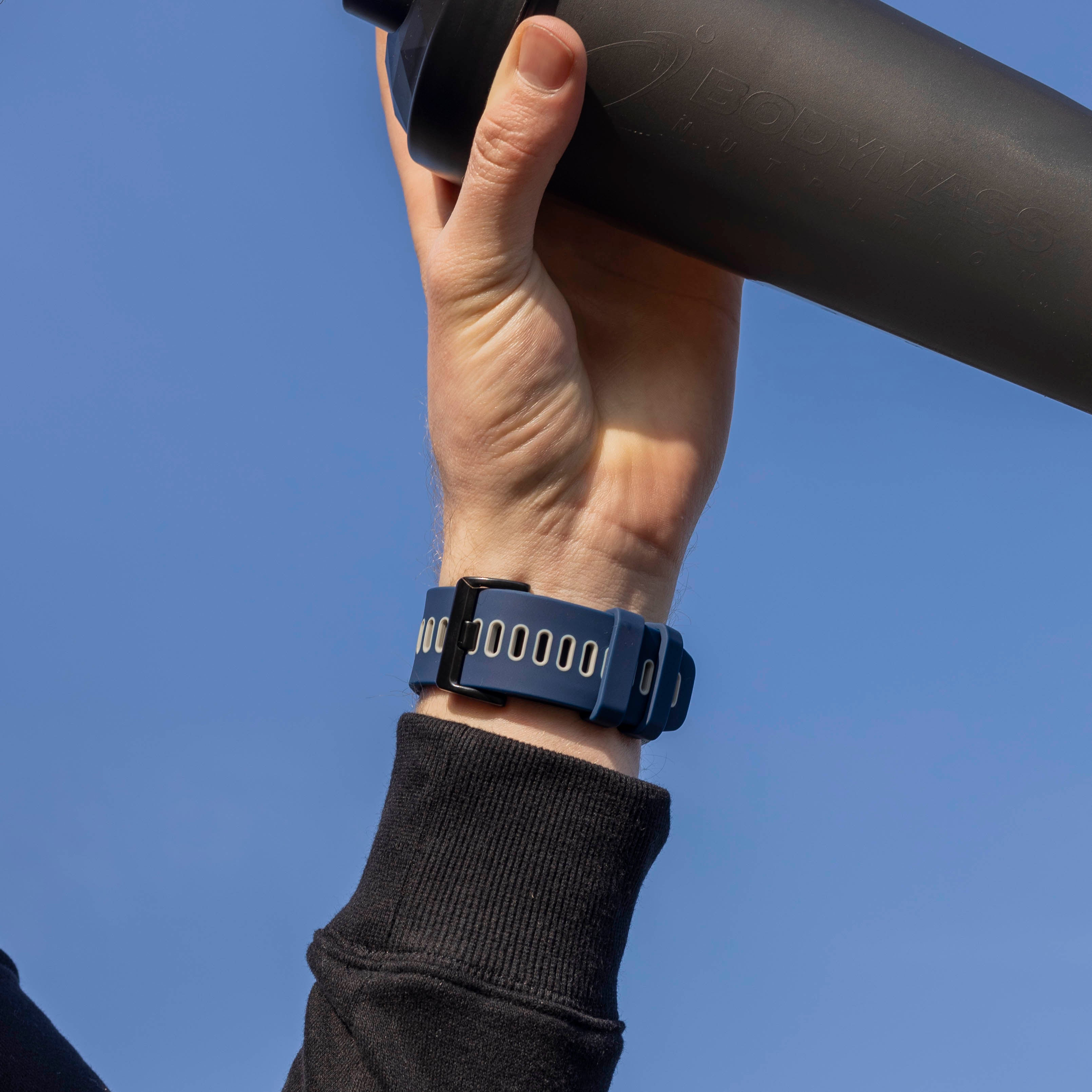 Eine Hand hält einen schwarzen Shaker. Am Handgelenk befindet sich eine blaue Uhr. Der Hintergrund ist ein klarer blauer Himmel.