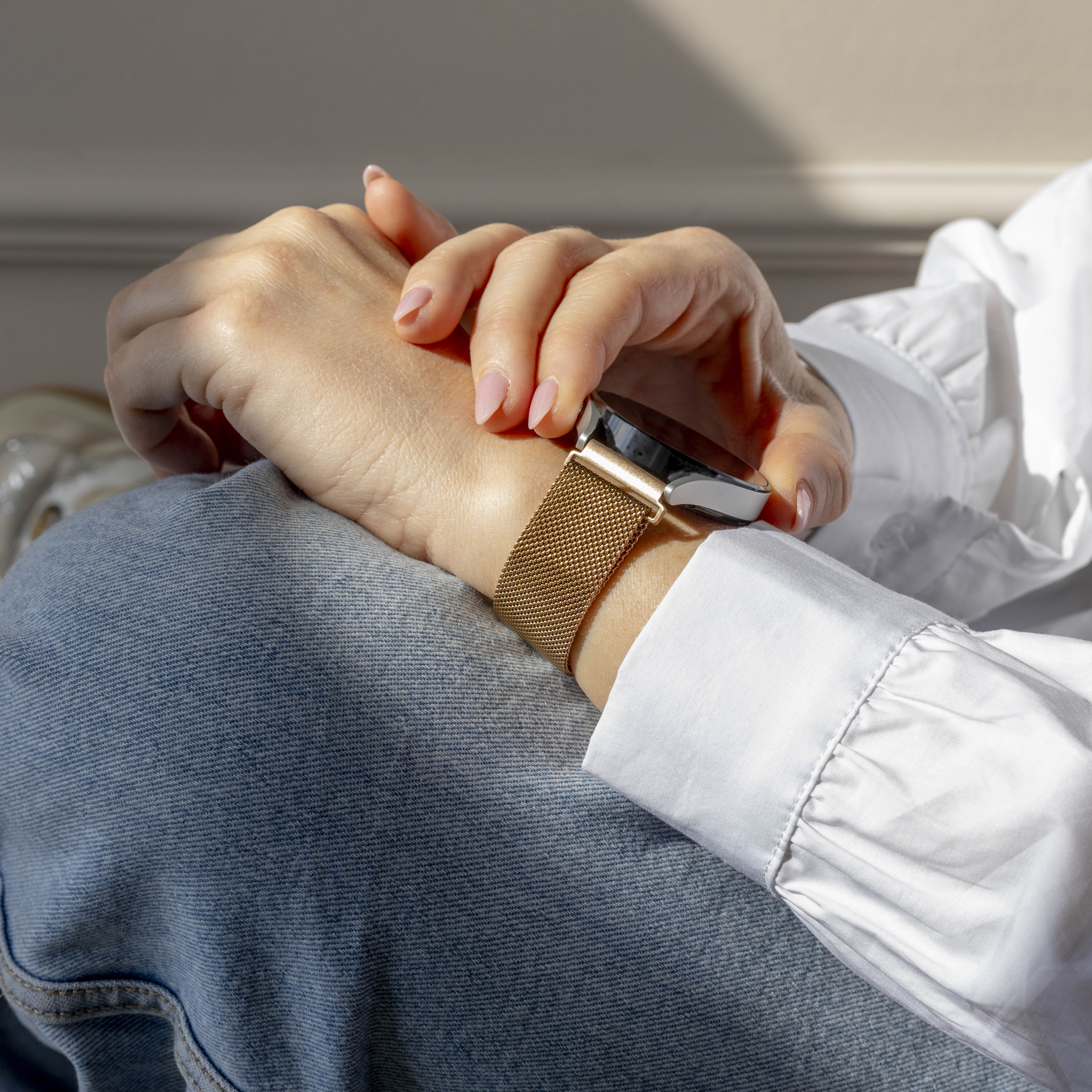 Hände einer Person mit goldener Uhr, weißem Hemd und blauer Jeans.