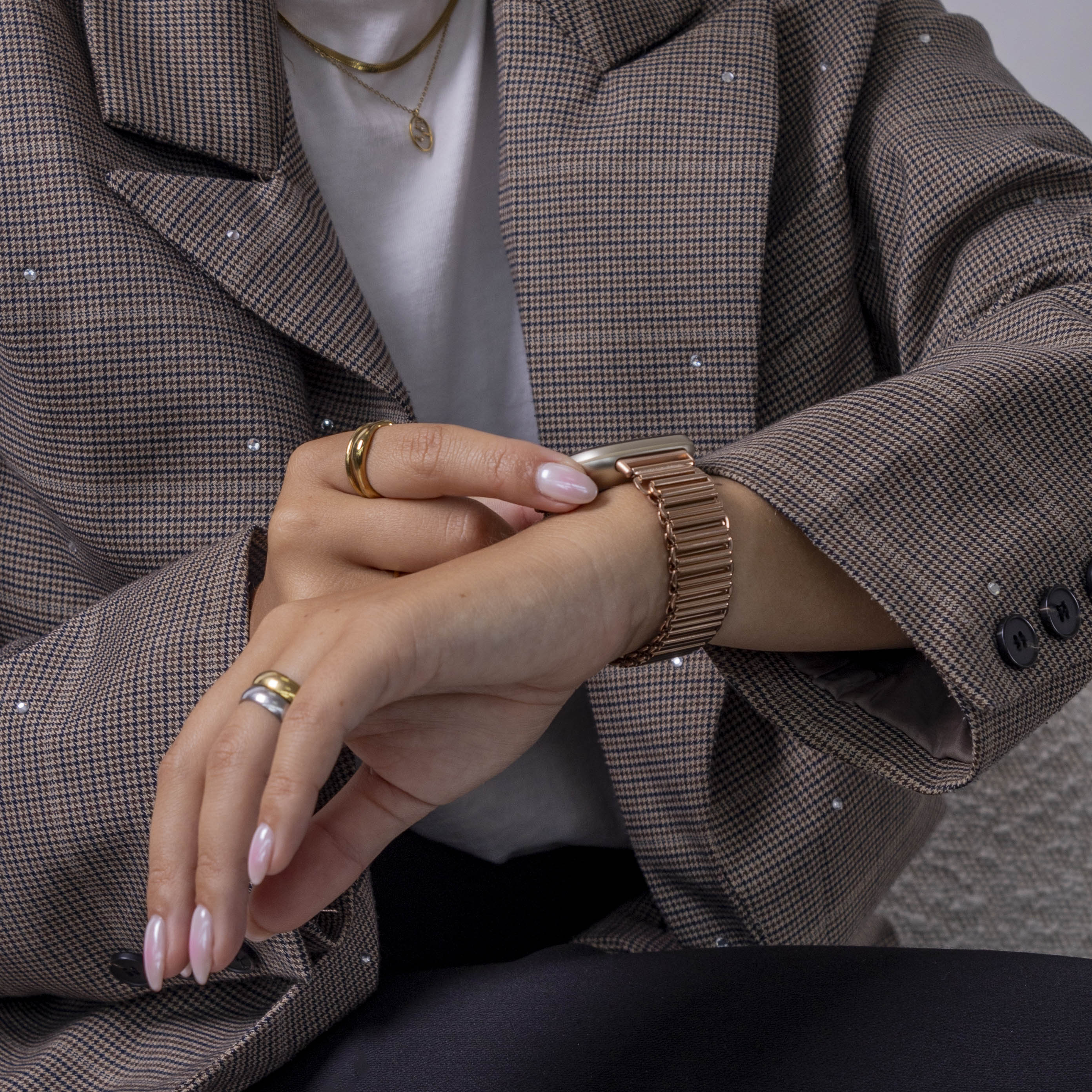 Eine Person mit braunem Blazer und Uhr. Sie trägt Ringe und ein weißes Hemd.