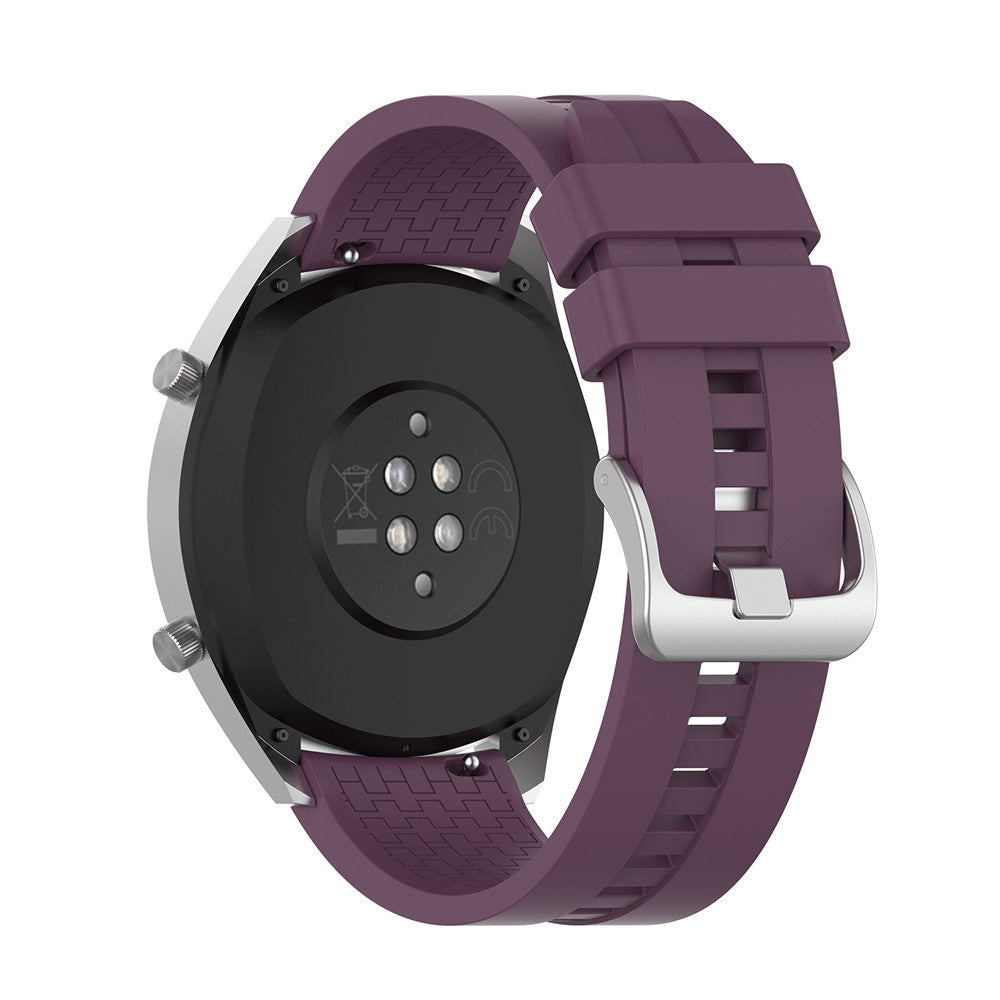 Eine Smartwatch mit lila Armband. Die Uhr hat ein silbernes Gehäuse und einen schwarzen Sensor auf der Rückseite. Der Riemen ist geschnallt.