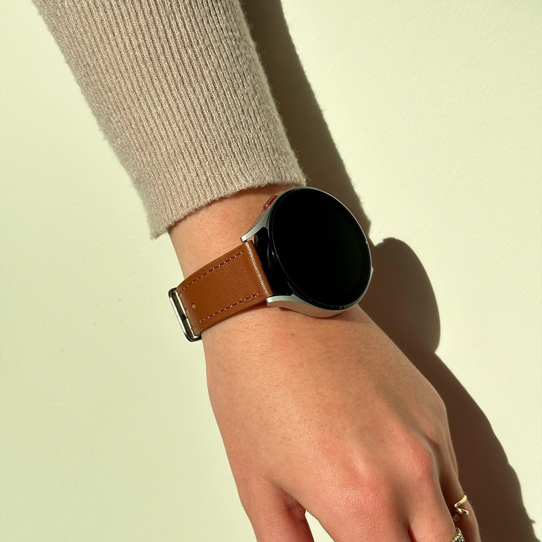 Ein Handgelenk mit einer braunen Lederuhr. Das Ziffernblatt ist schwarz. Die Person trägt einen beigen Pullover.