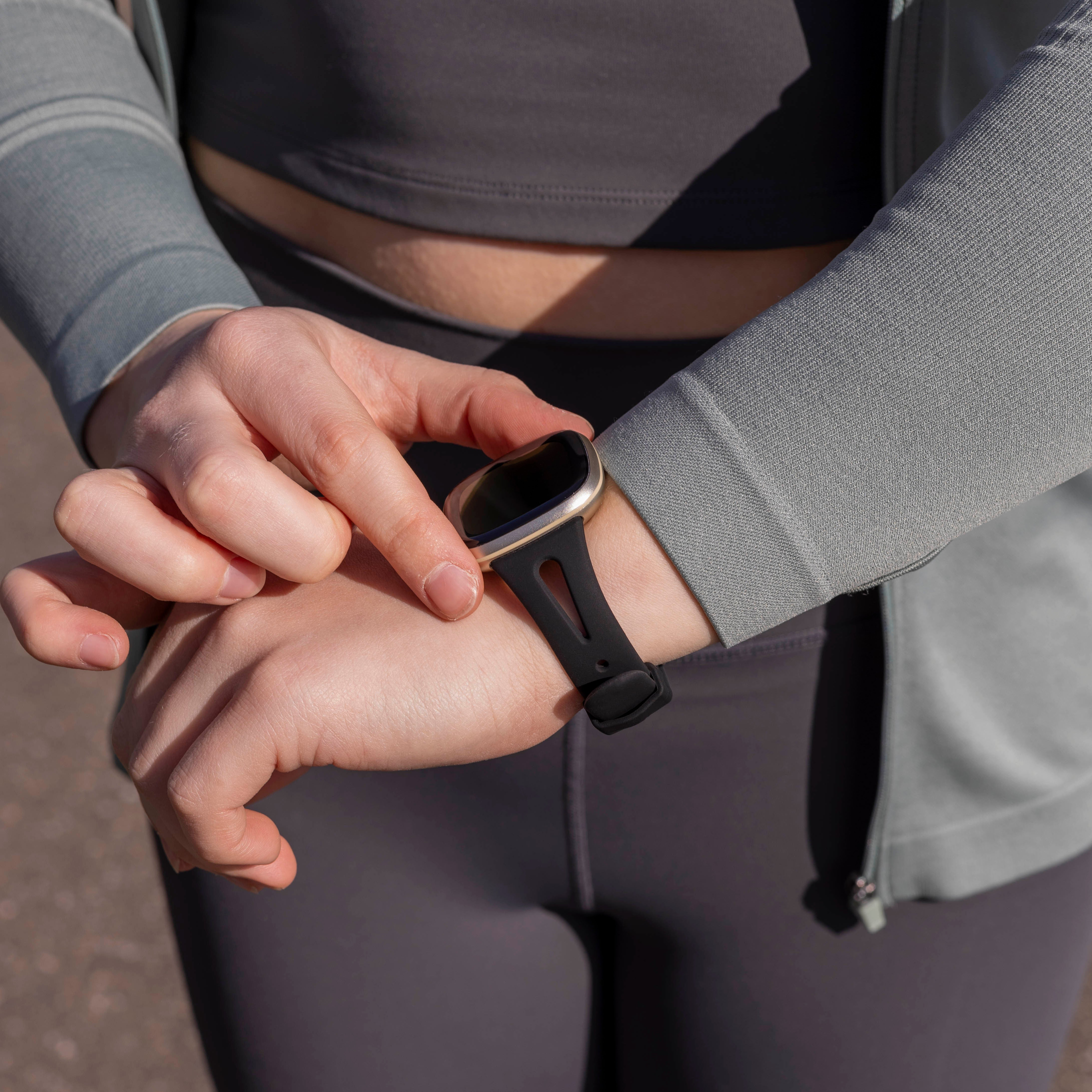 Eine Person mit Smartwatch. Sie überprüft die Uhr am Handgelenk und trägt graue Sportkleidung.