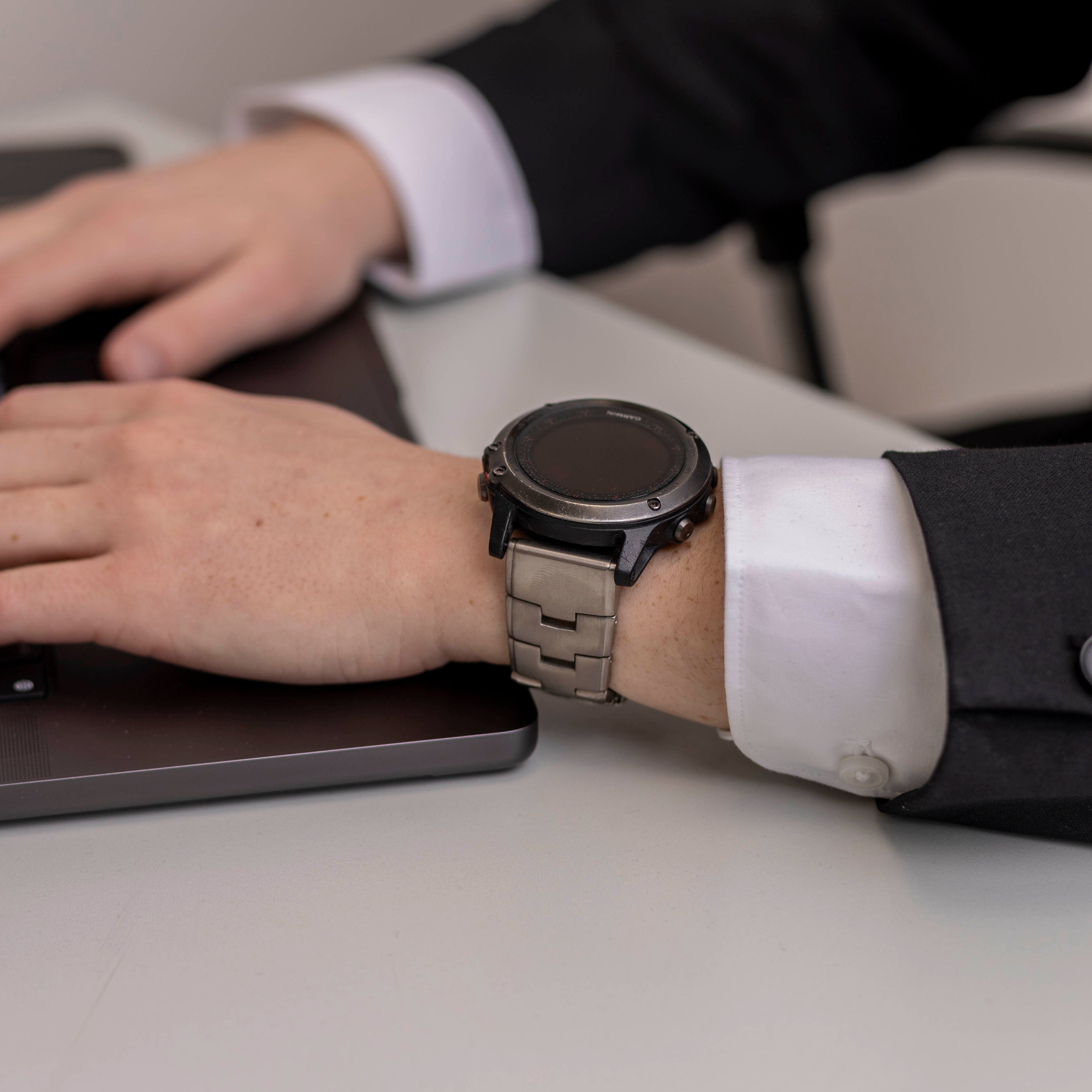 Eine Person, die beim Arbeiten an einem Laptop eine Smartwatch am Handgelenk trägt. Sie trägt ein weißes Hemd und einen schwarzen Anzug.