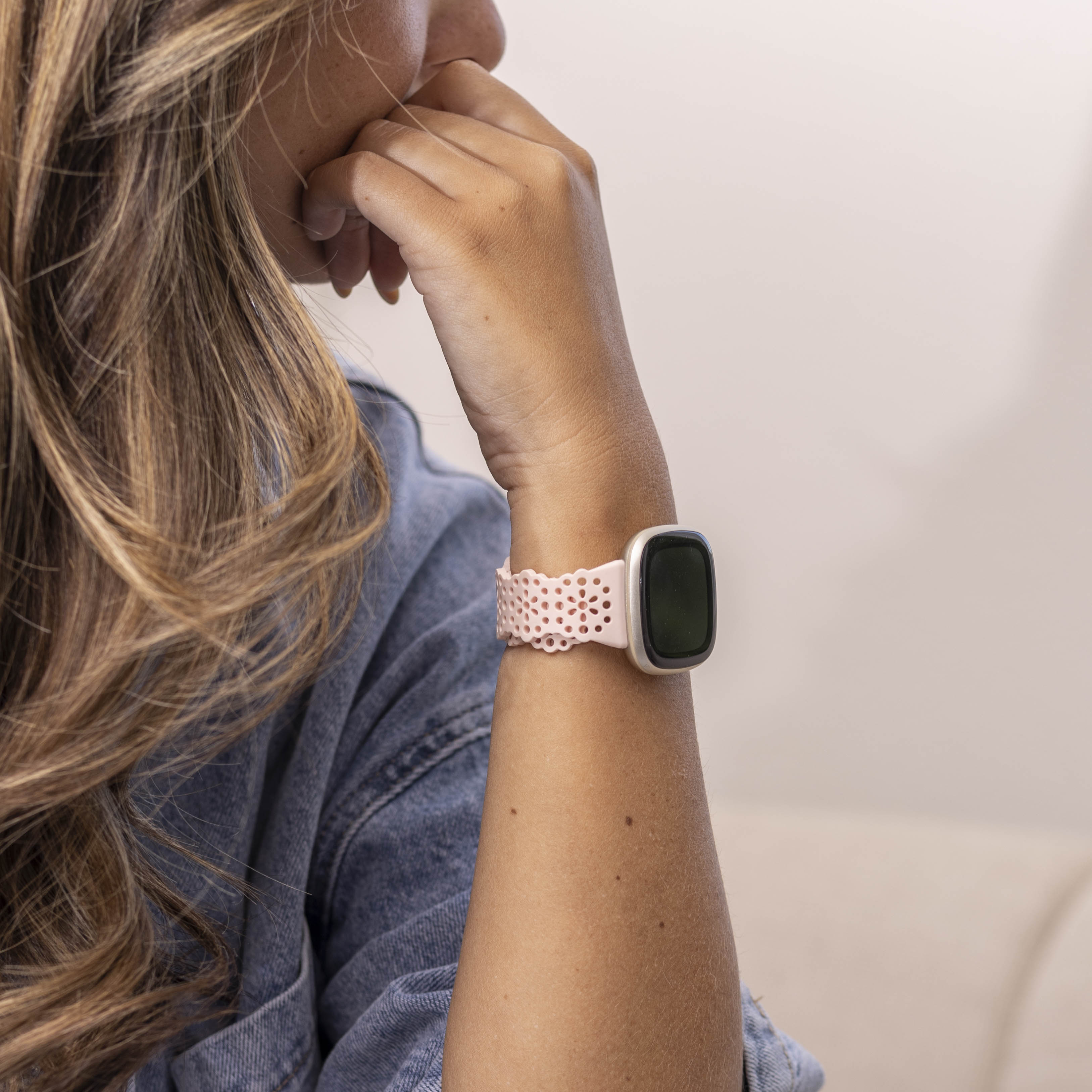 Eine Person, die eine rosa Smartwatch mit einem perforierten Armband trägt. Die Person trägt eine Jeansjacke.