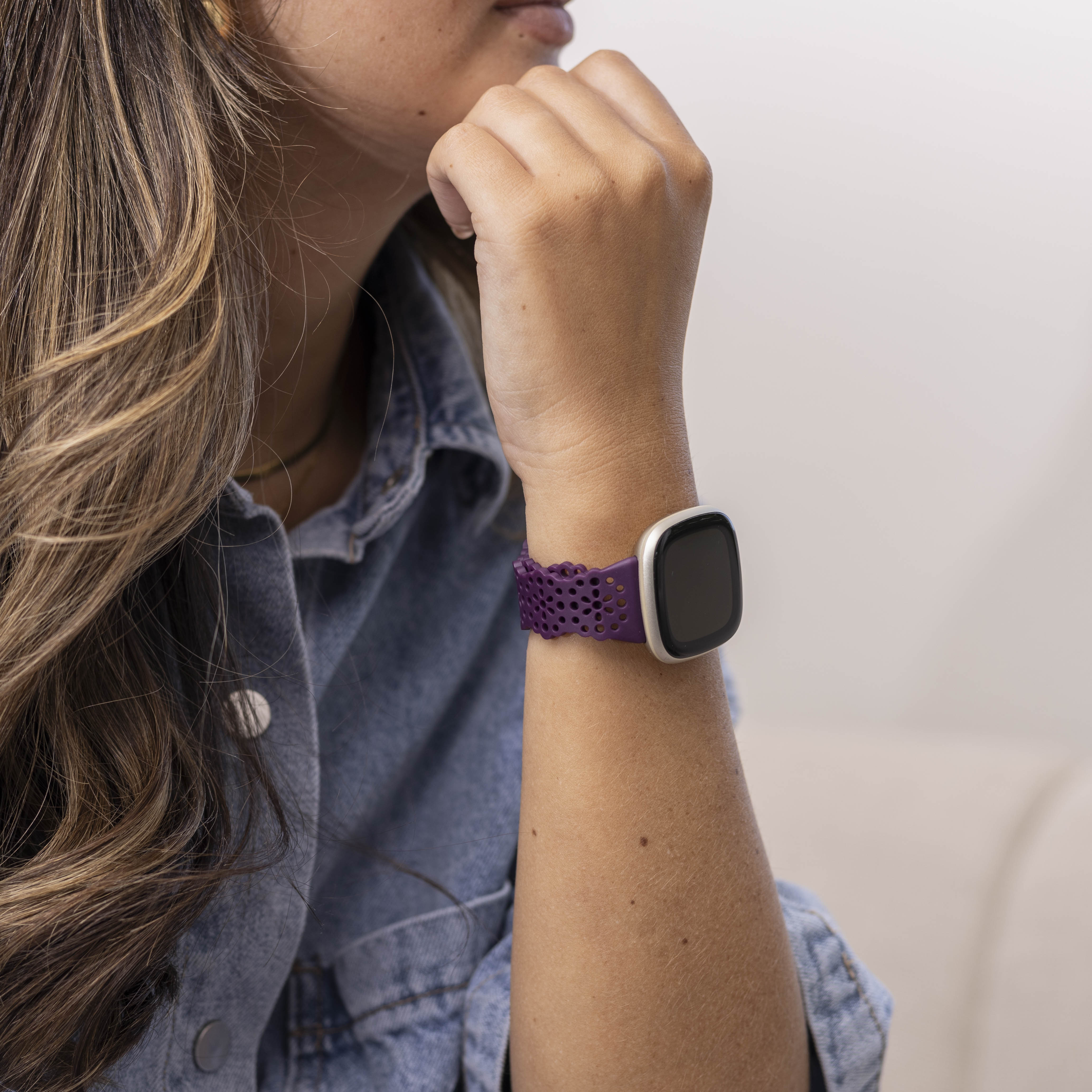 Arm einer Person mit lila Uhr und schwarzem Bildschirm. Die Person trägt eine Jeansjacke.