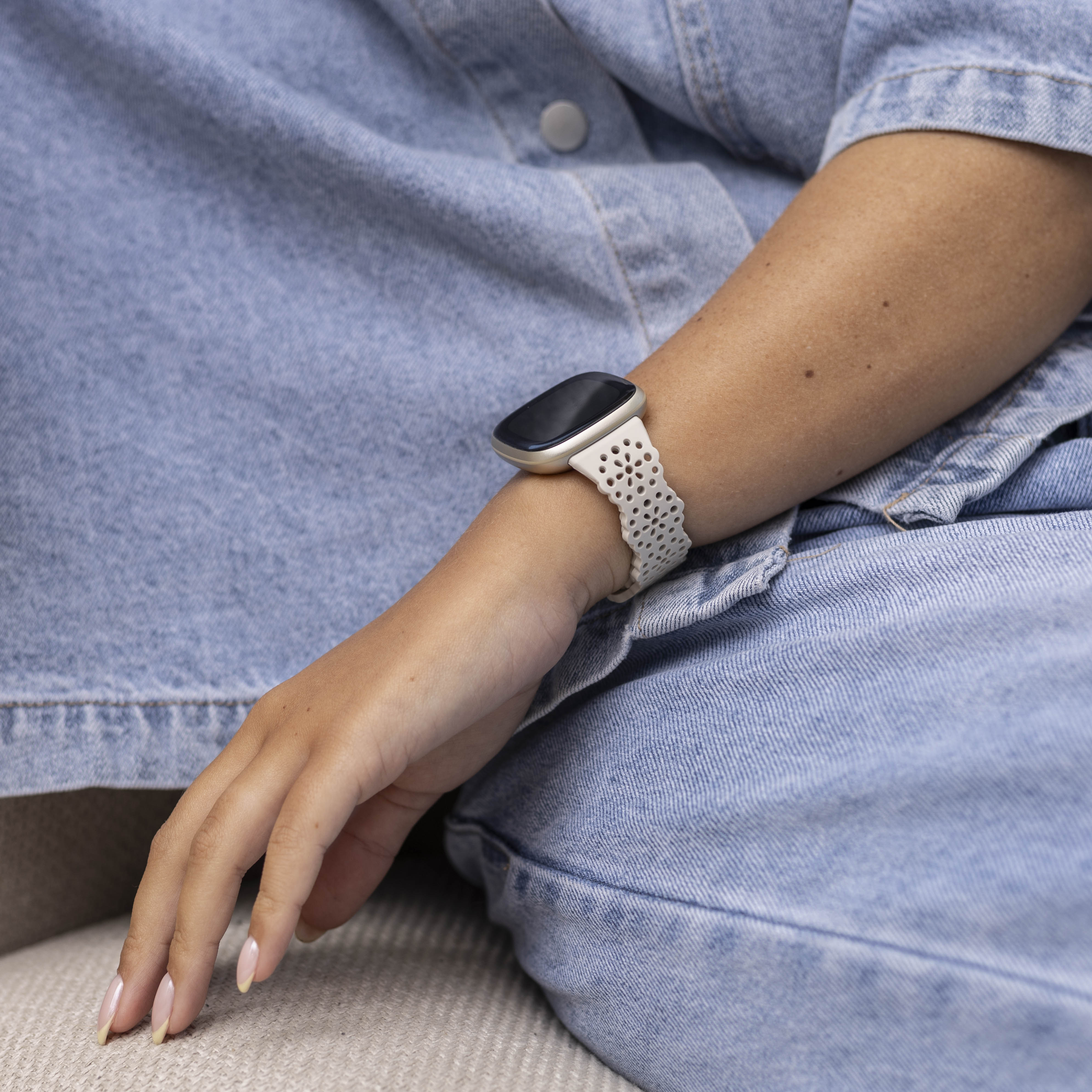 Ein Arm mit einer Smartwatch. Die Person trägt ein Jeanshemd. Der Arm liegt auf einem bein mit Jeansstoff.