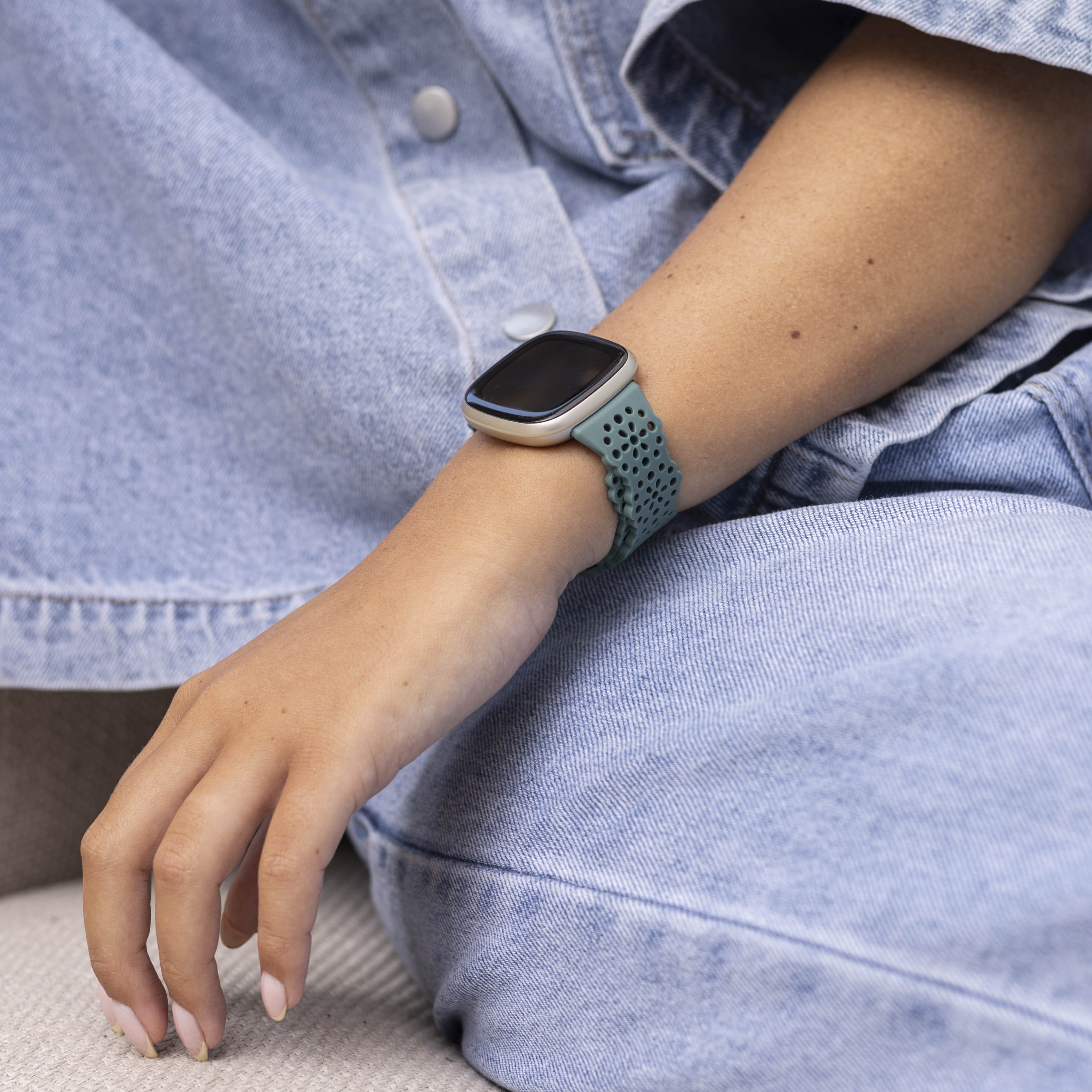 Arm einer Person mit Smartwatch und grünem Armband, auf Jeansstoff. Die Nägel sind lackiert.