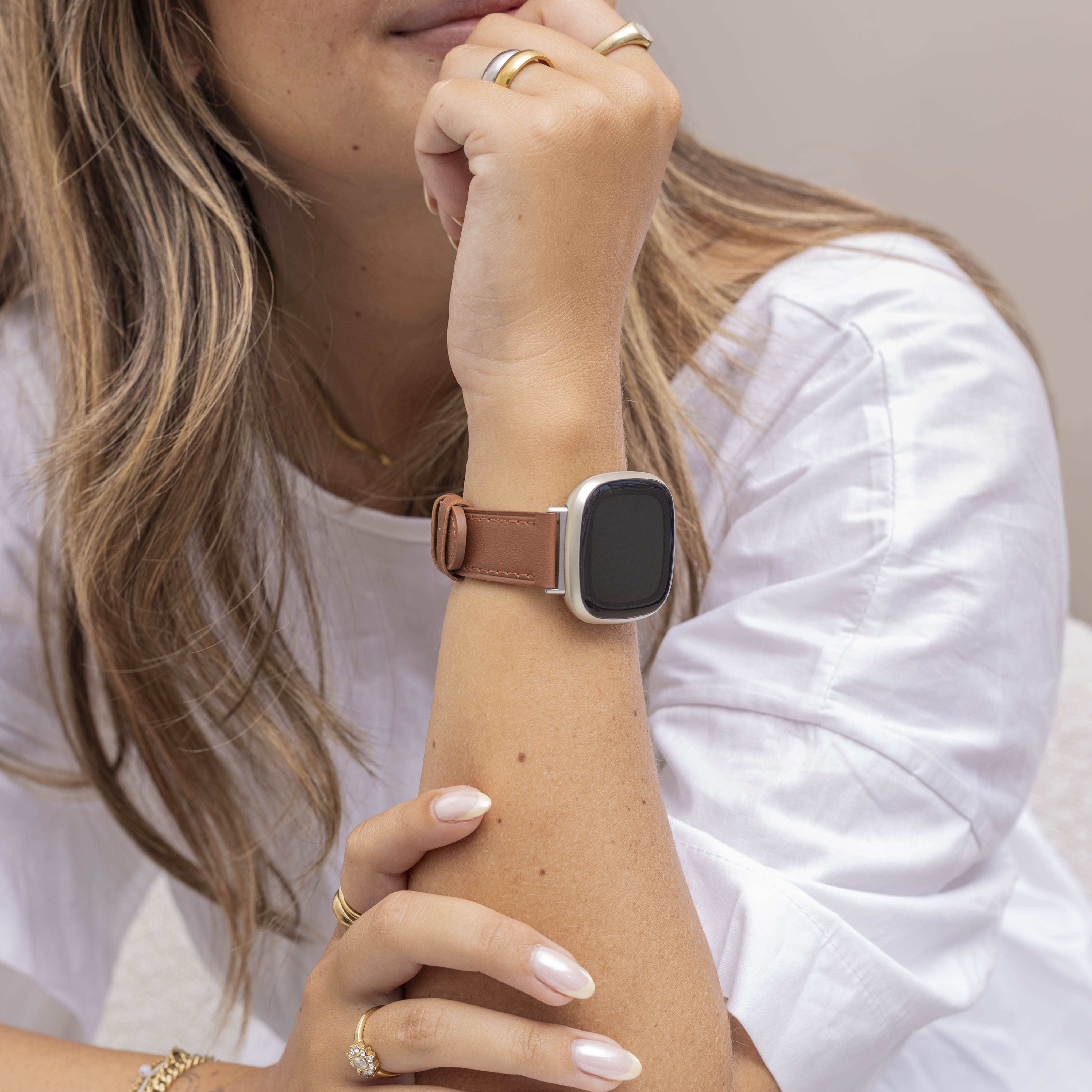 Arm einer Frau mit Uhr. Sie trägt Ringe und ein weißes Hemd. Die Uhr hat ein braunes Lederarmband.