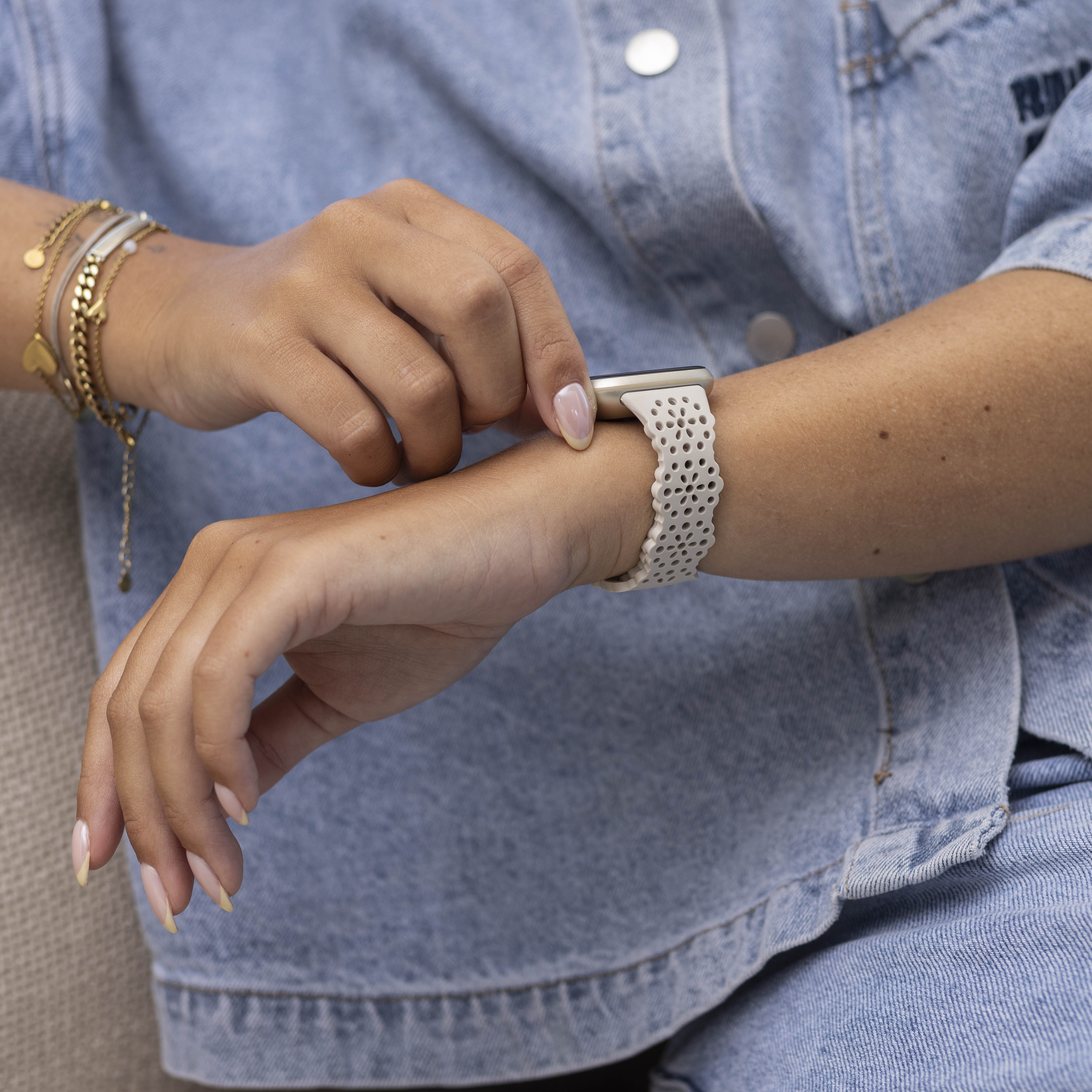 Eine Person justiert ihre Uhr. Sie trägt eine Jeansjacke und goldene Armbänder. Die Uhr hat ein helles Armband.