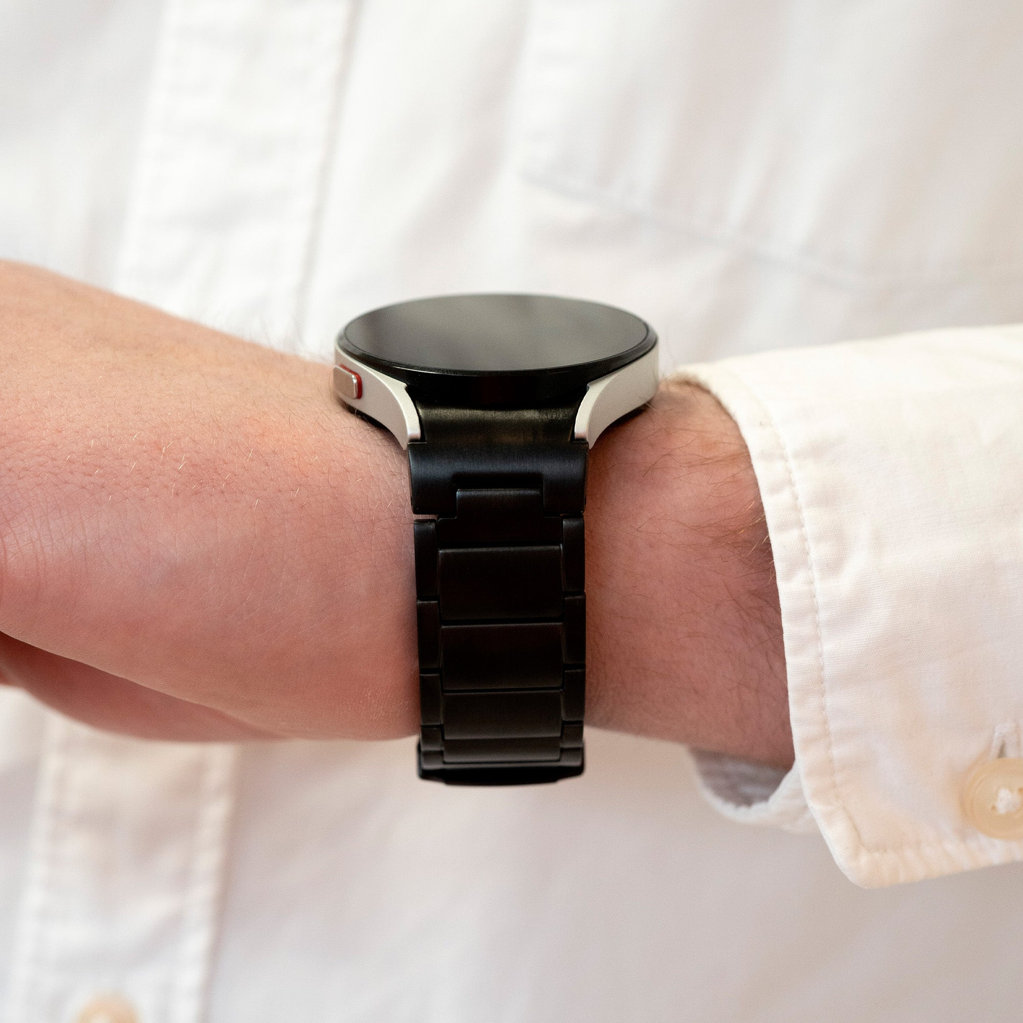 Eine schwarze Smartwatch mit schwarzem Metallarmband am Handgelenk einer Person. Die Person trägt ein weißes Hemd.