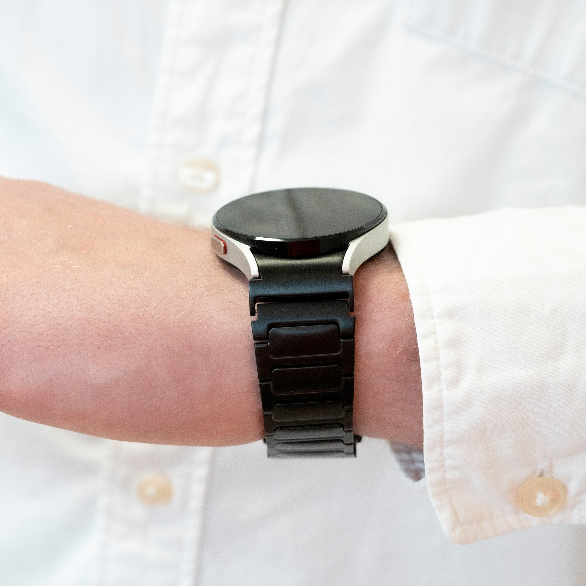 Eine Person trägt eine schwarze Smartwatch am Handgelenk. Die Person trägt ein weißes Hemd.