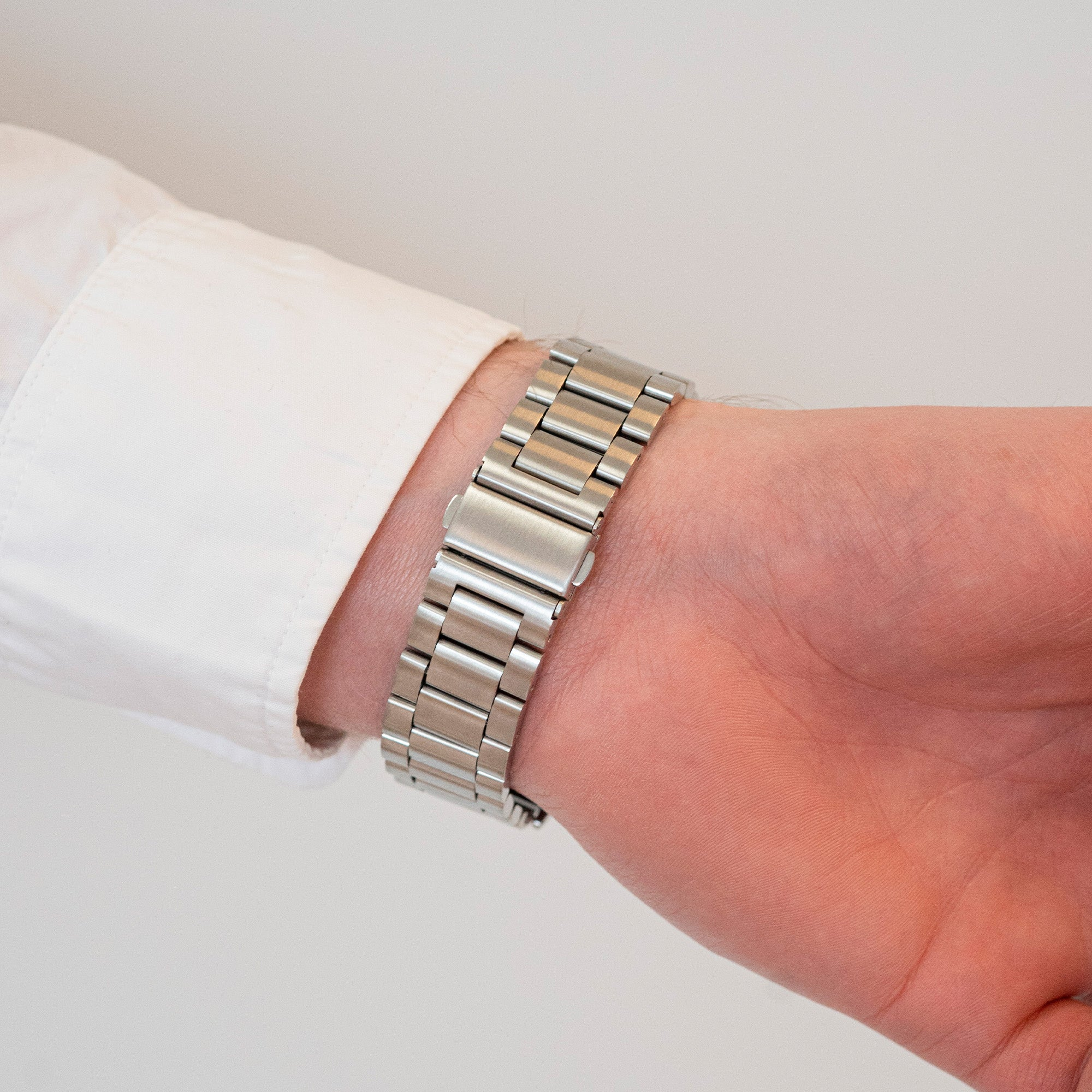 Das Handgelenk einer Person mit einer silbernen Uhr. Die Person trägt ein weißes Hemd. Der Hintergrund ist schlicht und weiß.