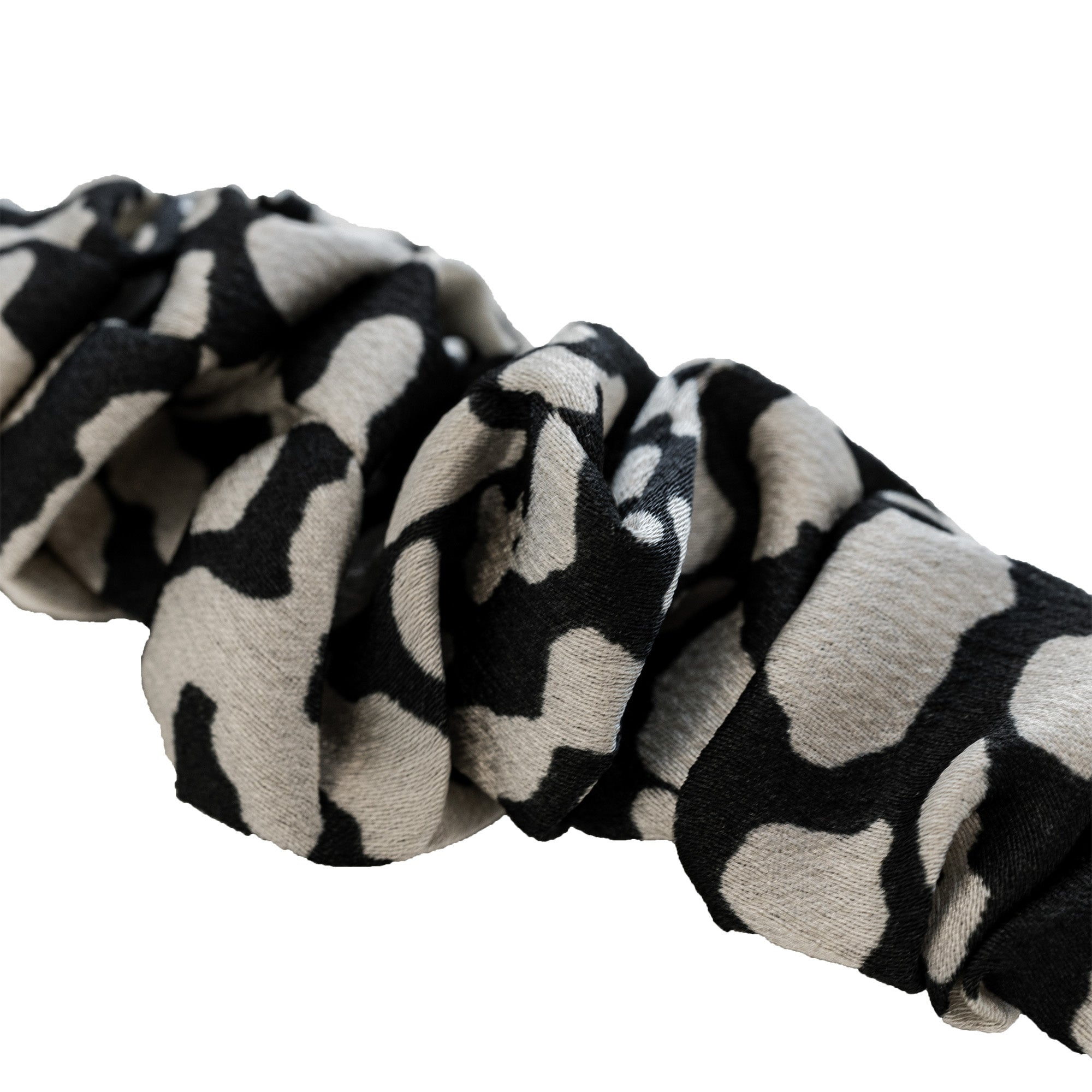 Ein schwarz-weiß gemustertes Scrunchie. Das Scrunchie besteht aus Stoff mit unregelmäßigen schwarzen Flecken auf hellgrauem Grund.