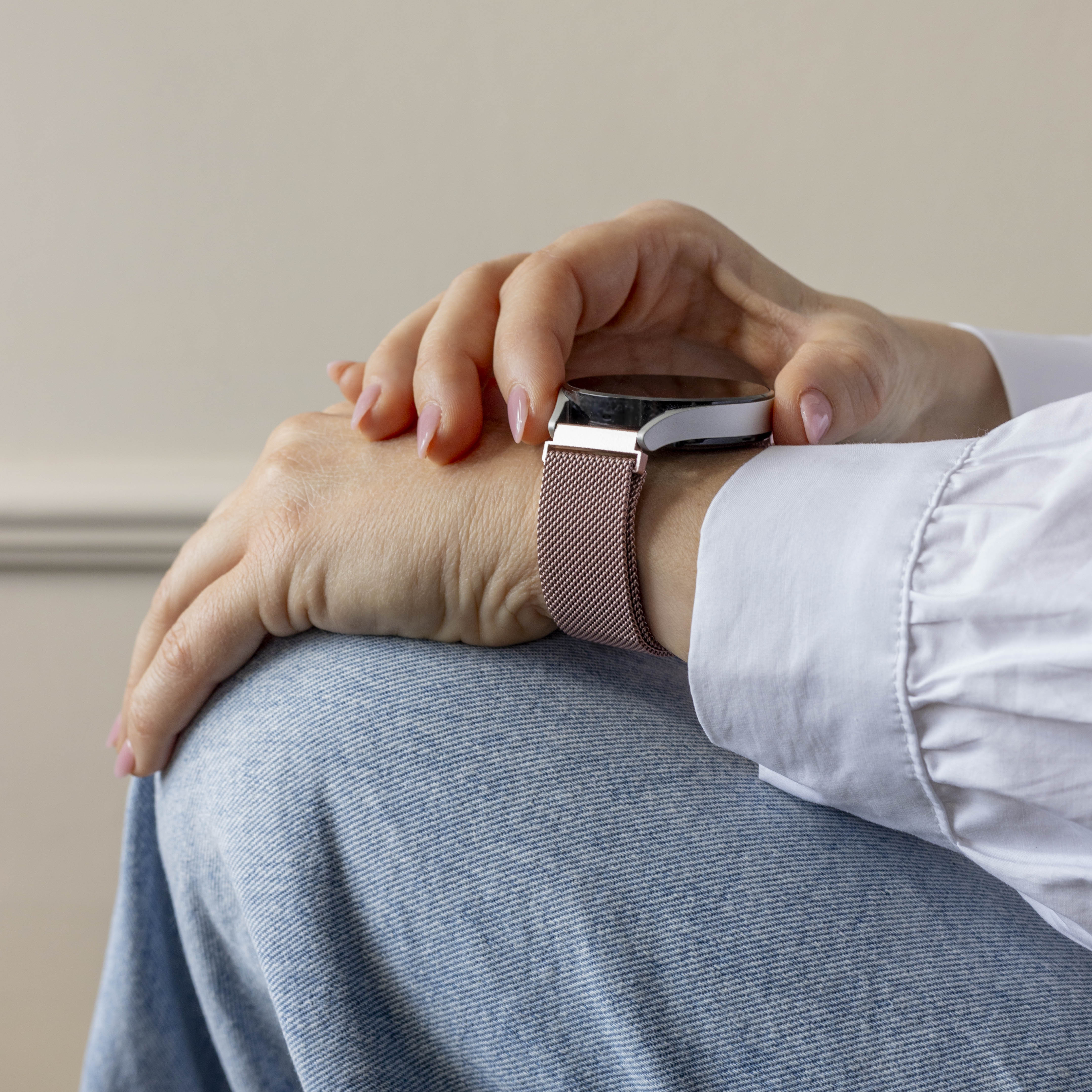 Eine Person trägt eine Smartwatch mit roségoldenem Armband. Die Person trägt ein weißes Hemd und Jeans.